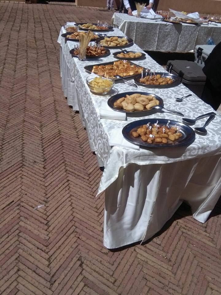 Tavolo di antipasti all'aperto, disposto su un lungo tavolo con una tovaglia bianca. Sullo sfondo un pavimento di mattoni.