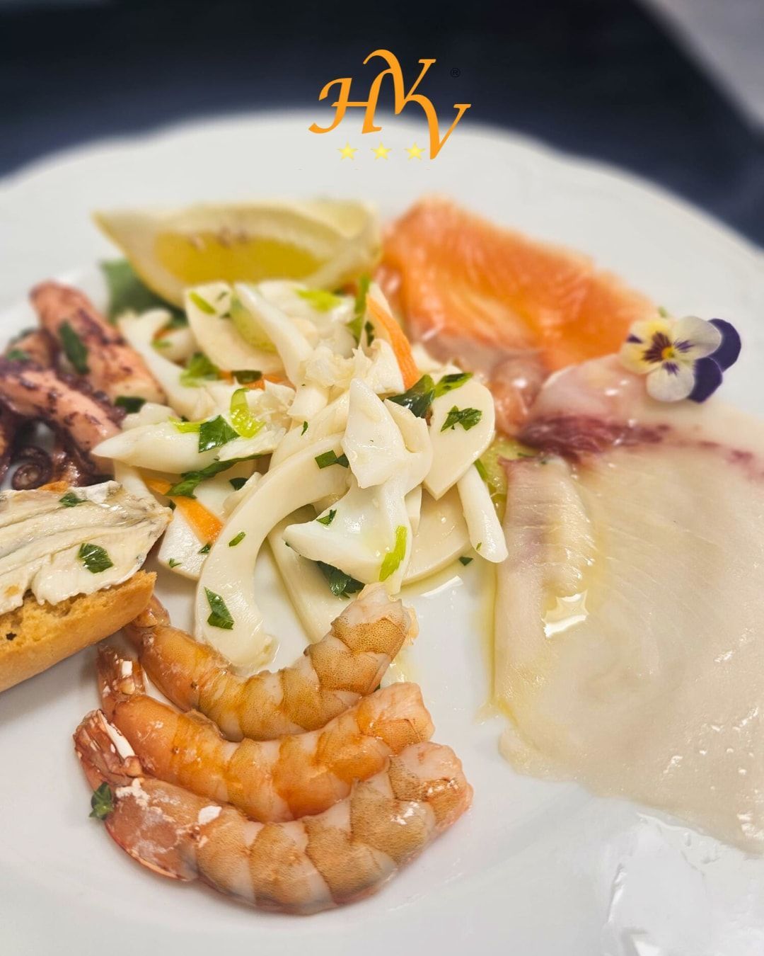 Piatto di antipasti di mare con gamberi, calamari, salmone e pesce bianco, guarnito con limone ed erbe aromatiche.