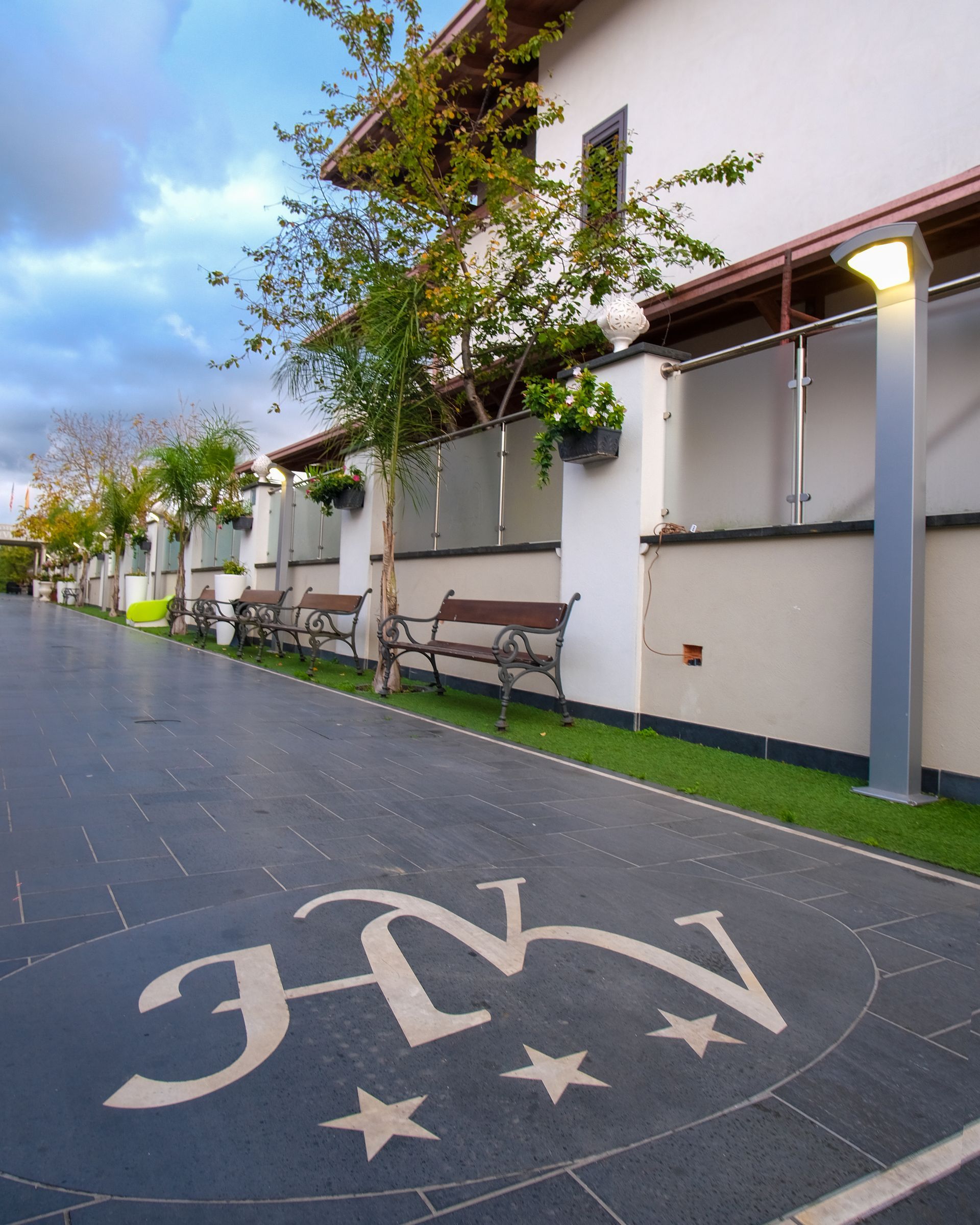 Esterno di un edificio con panchine, verde e un logo sul marciapiede.