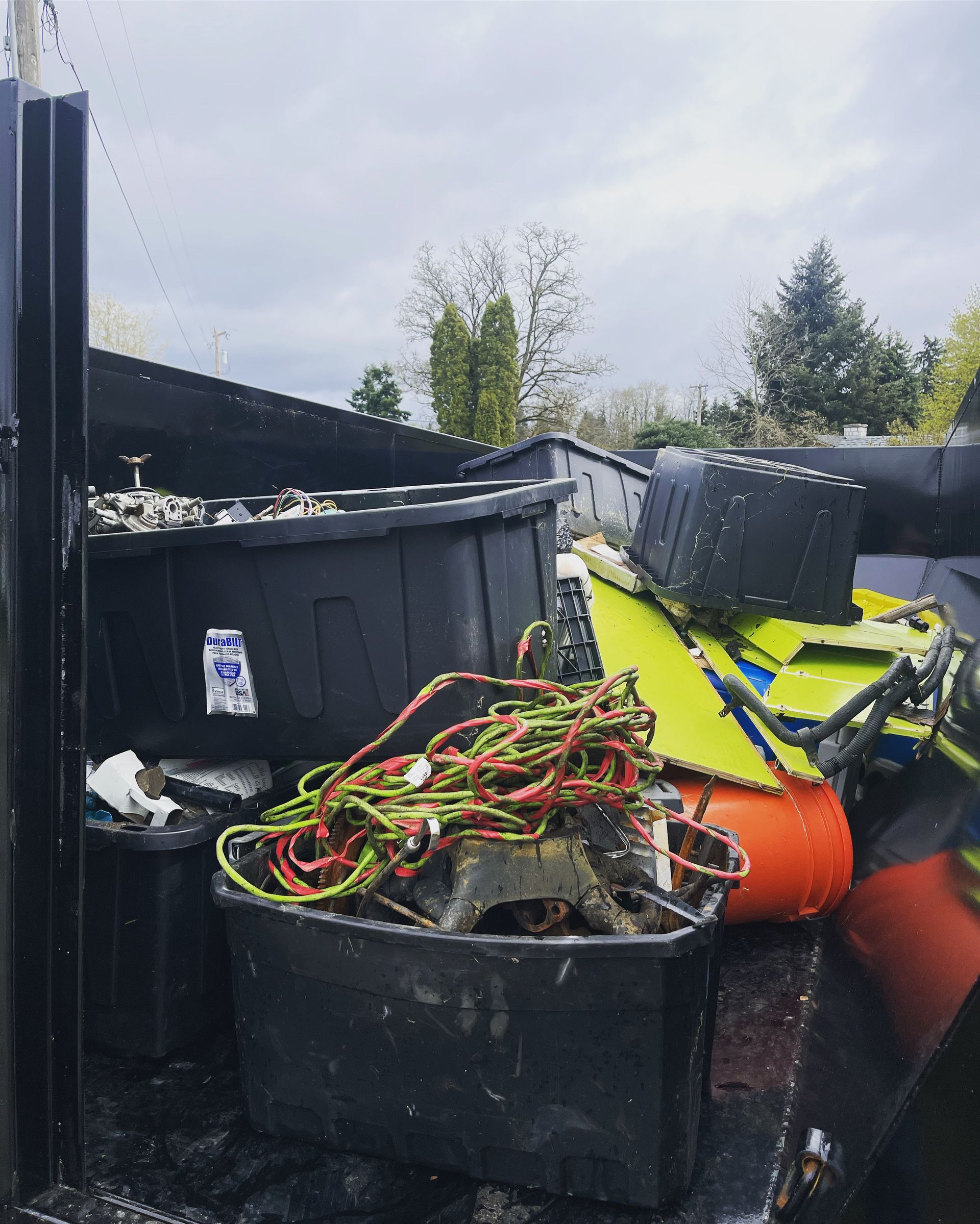 A truck bed filled with debris, including black bins and tangled wires.