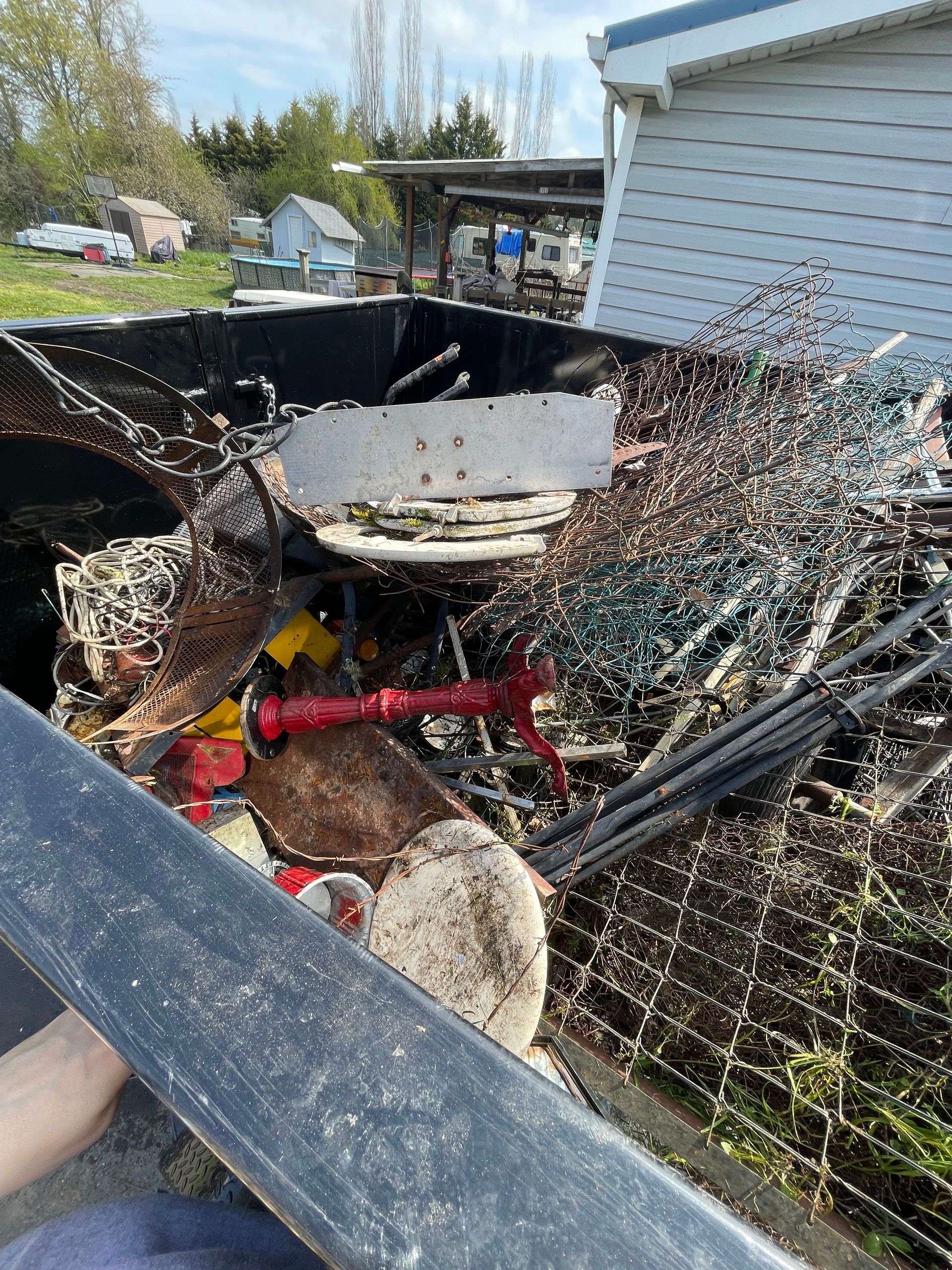 A truck bed overflowing with scrap metal, including wires, grates, and other discarded items, outdoors on a sunny day.