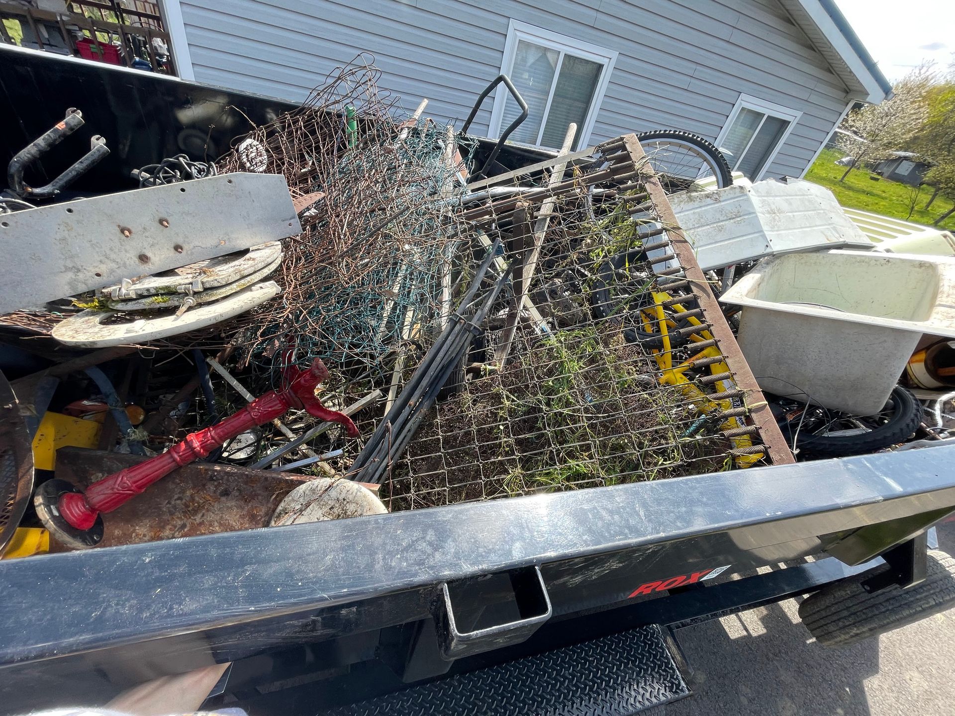 Truck bed overflowing with scrap metal and debris outside a house.