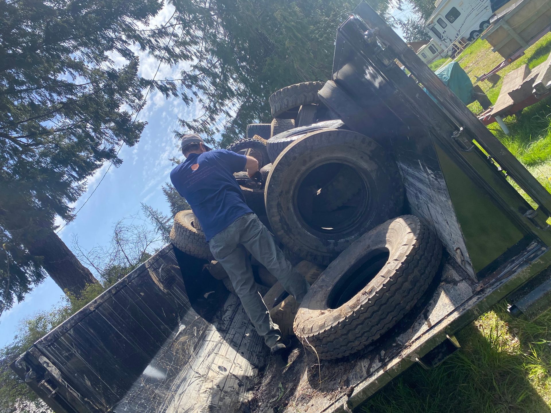 A man standing on a trailer, loading tires under a sunny sky.