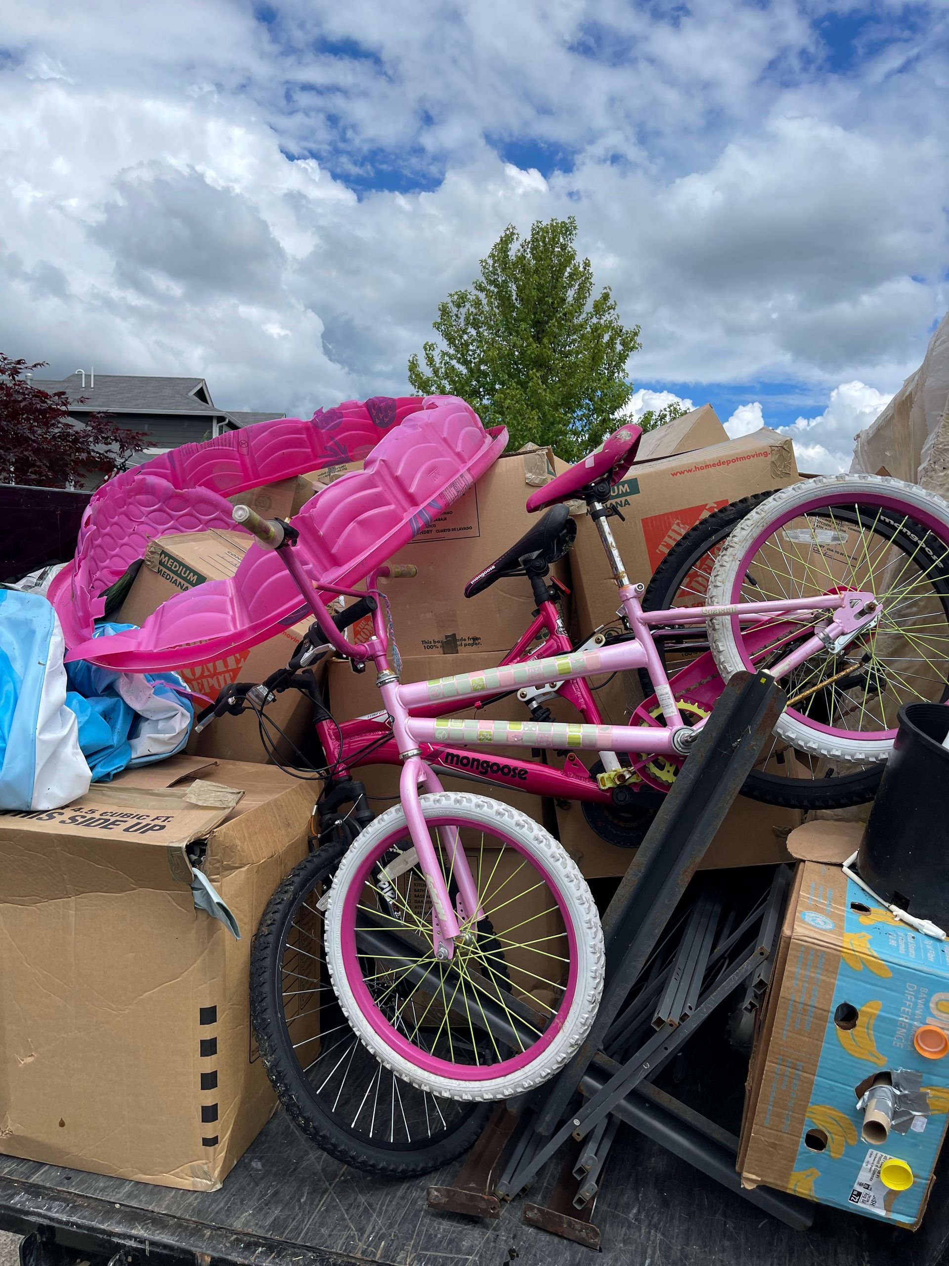 Pile of moving boxes and a pink bicycle in the back of a truck on a cloudy day.