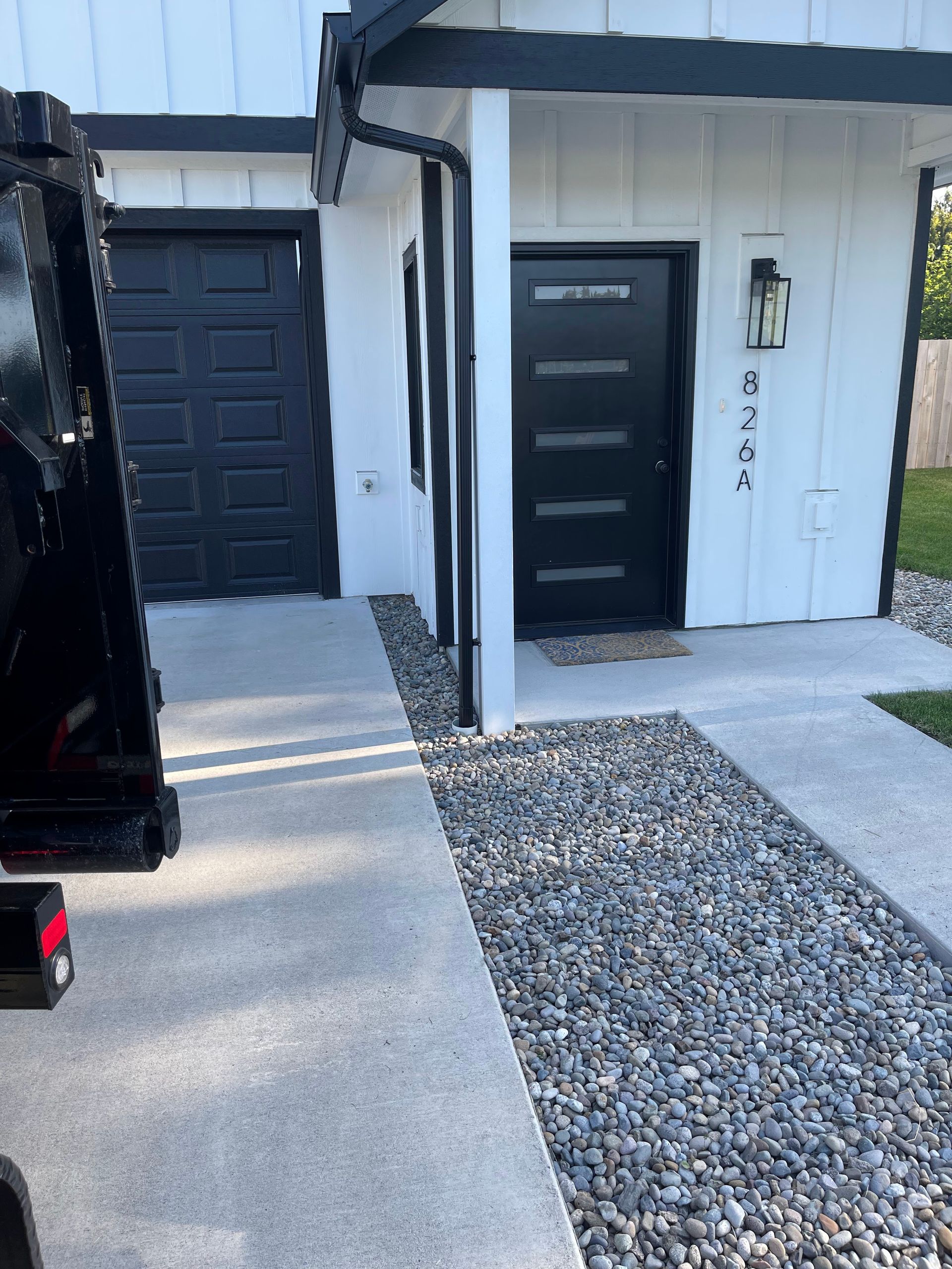 Exterior view of a white house with a black door, garage, and trim. A concrete path leads to the entrance.