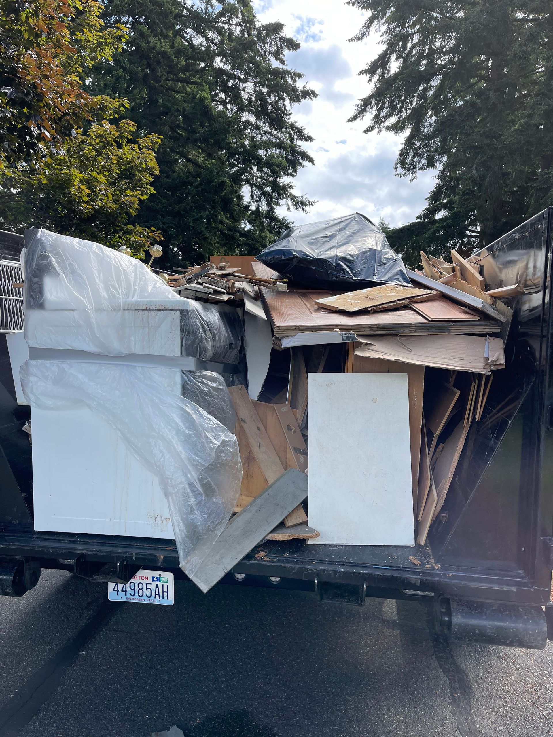 Dumpster filled with construction debris, including white panels, wood, and tarp.