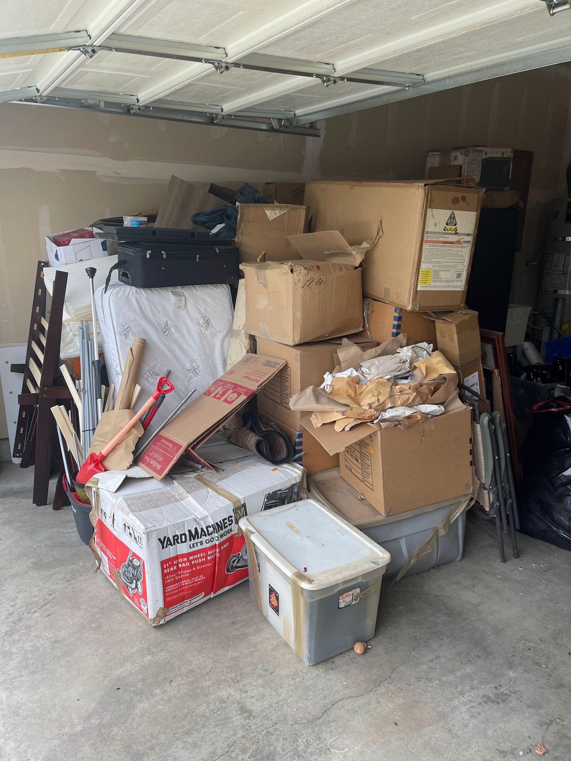 Cluttered garage filled with cardboard boxes, furniture, and storage bins.