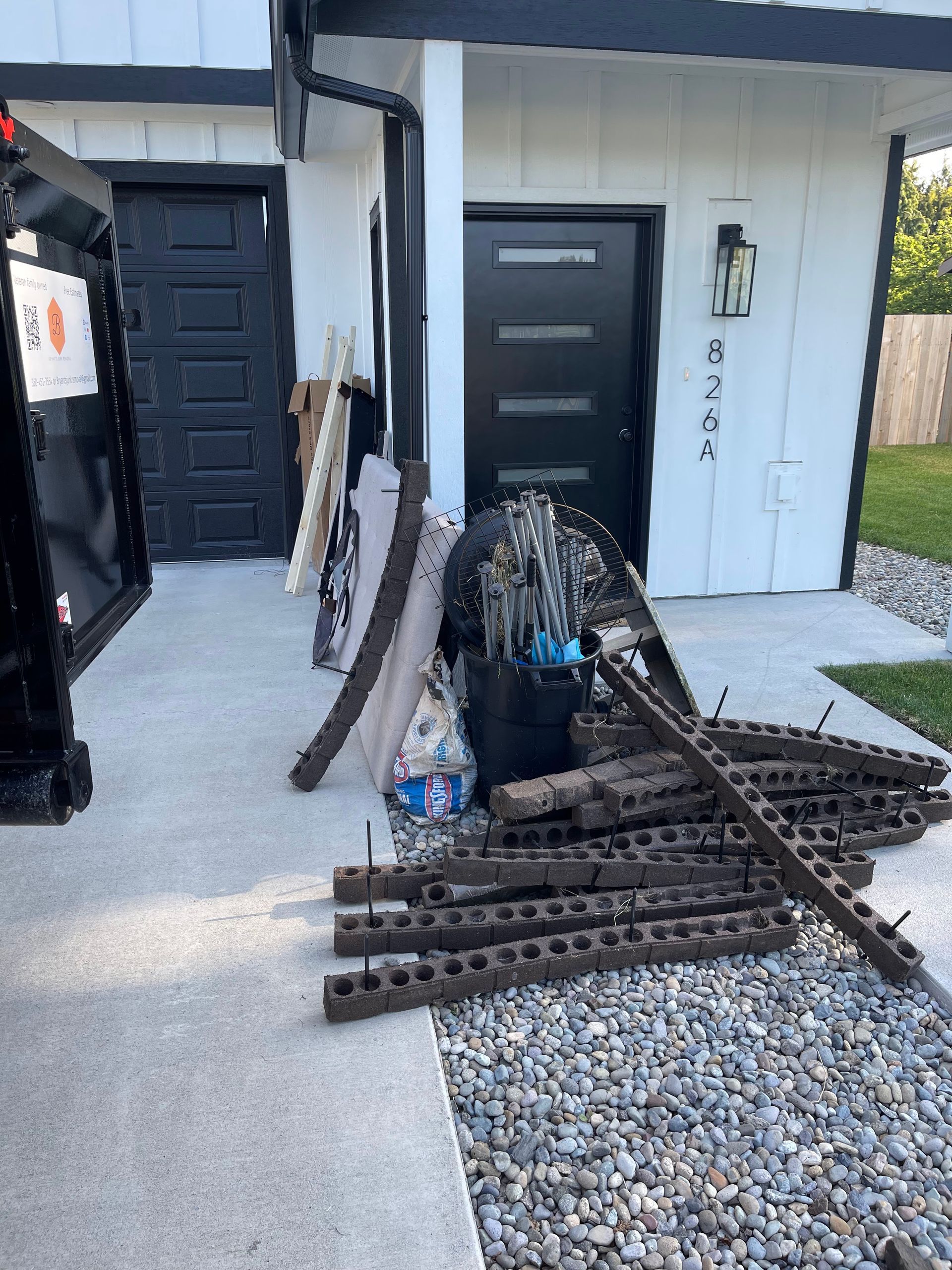 Exterior of a house with debris piled on the sidewalk. Black door, white walls, and grass are visible.
