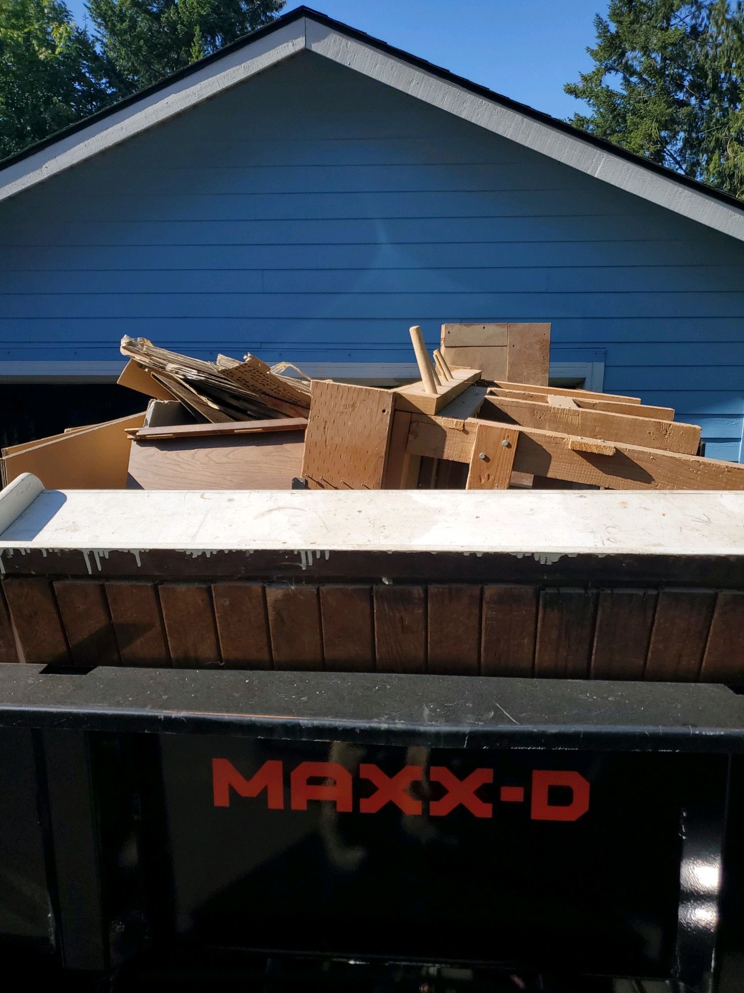 A truck bed filled with brown construction debris in front of a blue house. The truck says 