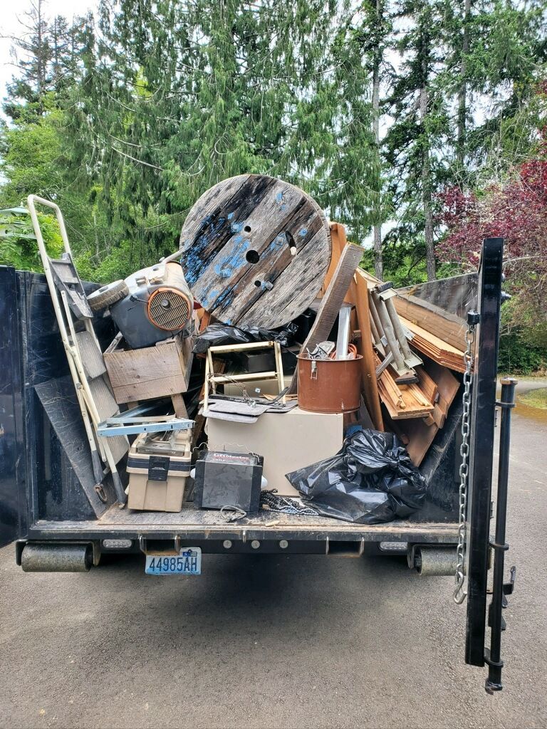 Dumpster filled with debris, including a large wooden spool and construction materials, outdoors.