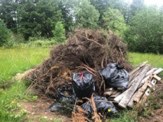 A pile of brush and black trash bags on the edge of a grassy field.