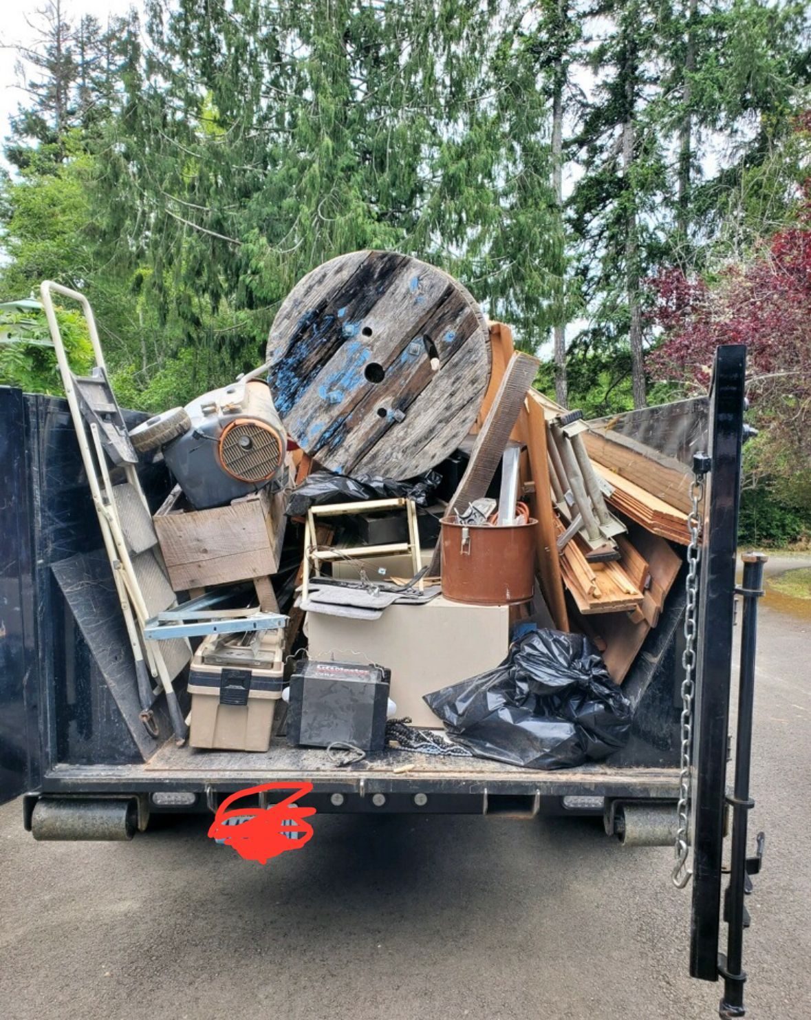 Truck bed filled with junk, including a large wooden spool, tools, and trash bags.