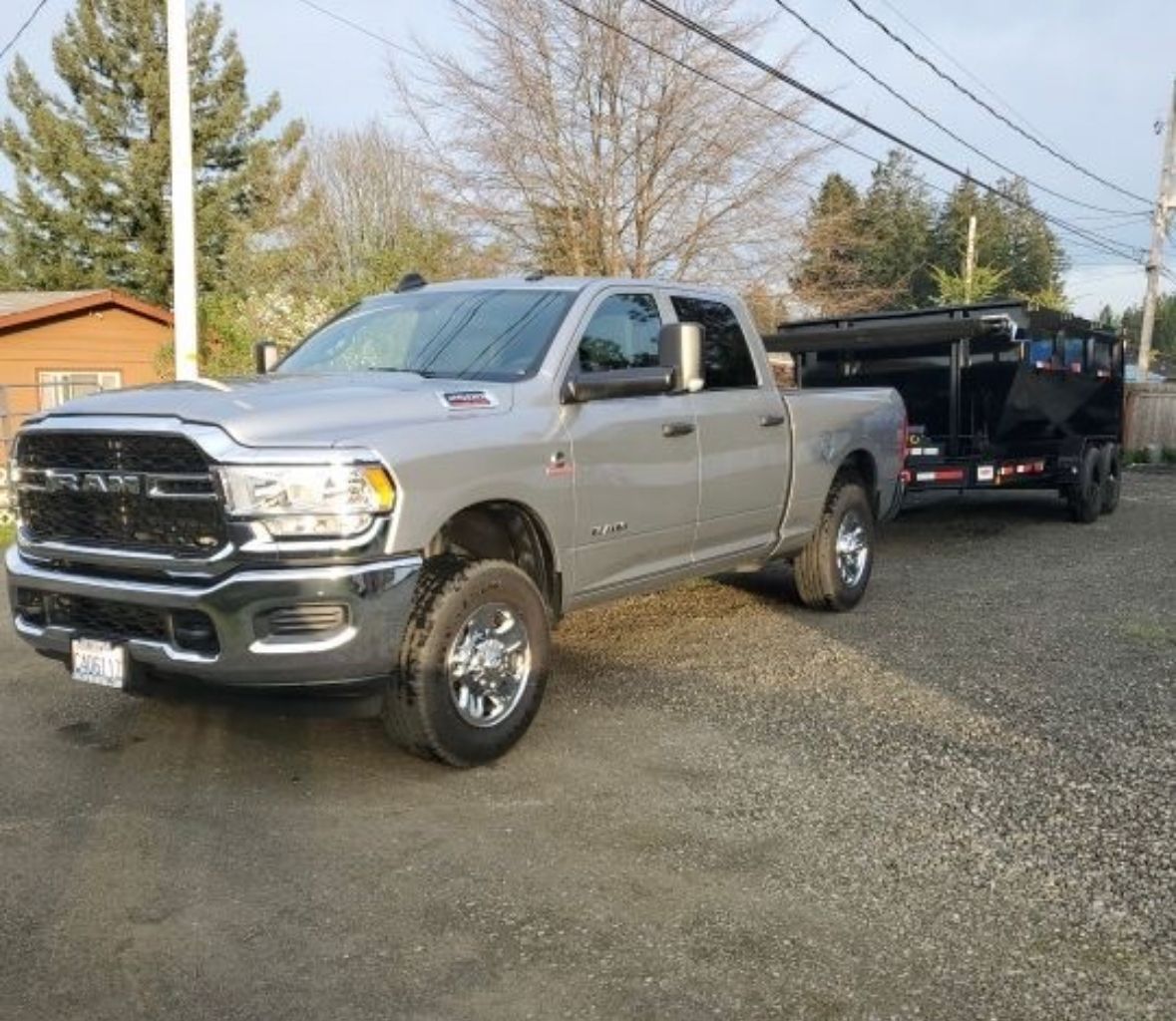 Silver Ram truck towing a black trailer on gravel.