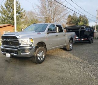 Silver Ram truck towing a black trailer on gravel.