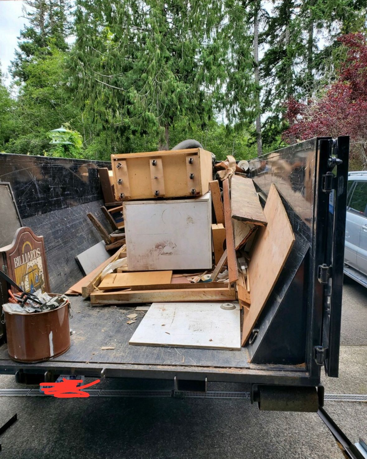 A dumpster filled with wooden furniture, boards, and debris sits outside, trees in the background.