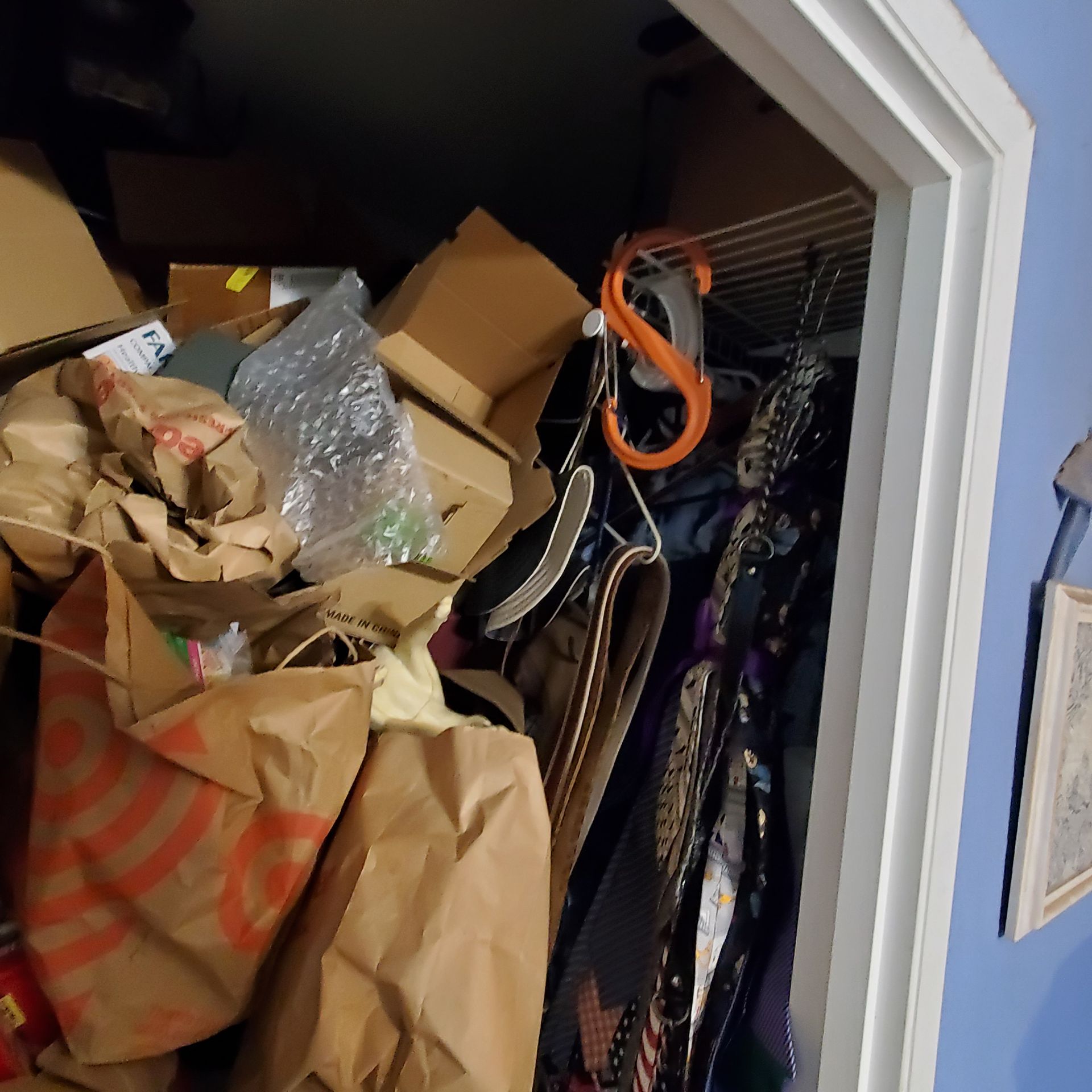 Cluttered closet with stacked boxes and clothes hanging, brown paper bags in front.