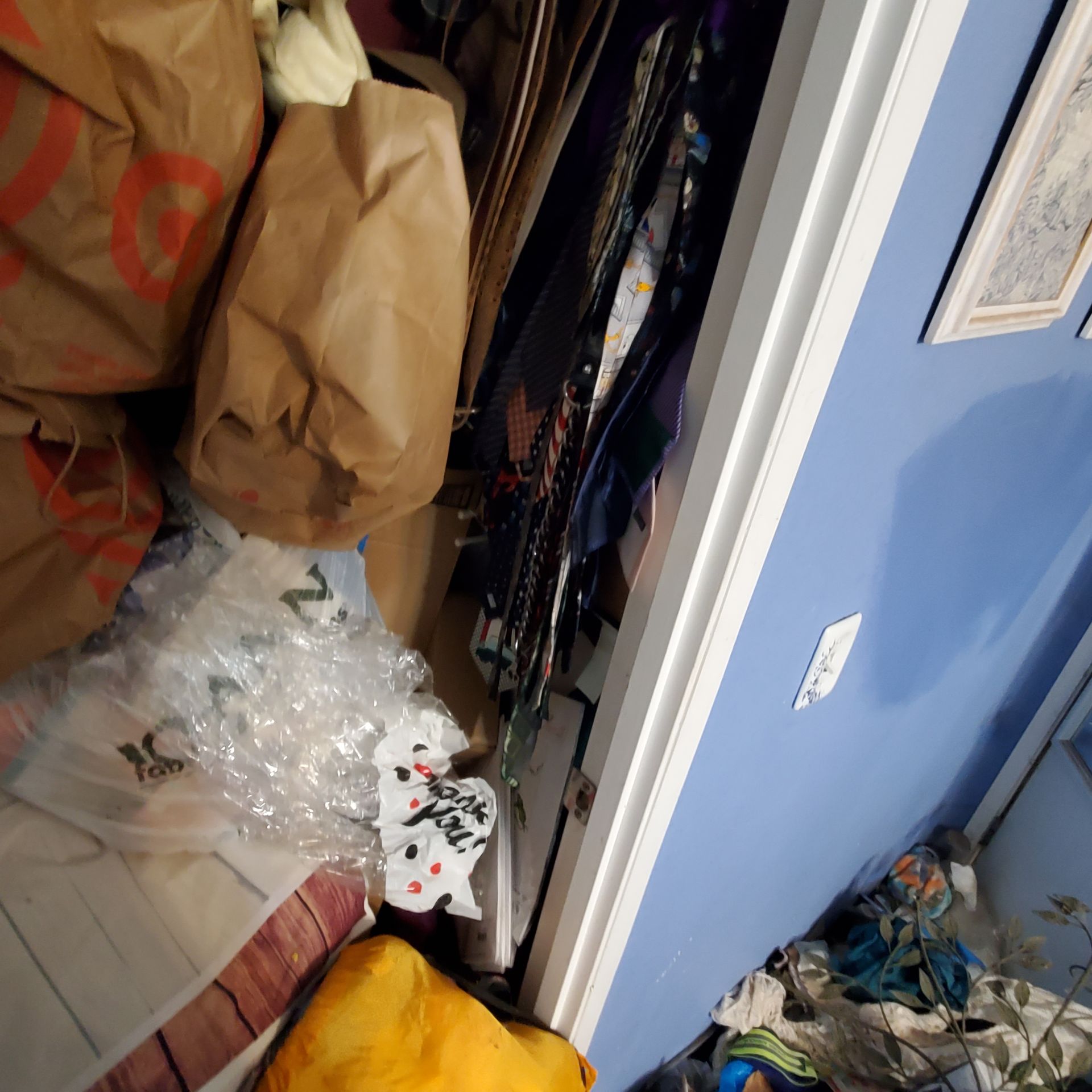Cluttered closet with brown paper bags, clothes, and a light blue wall.