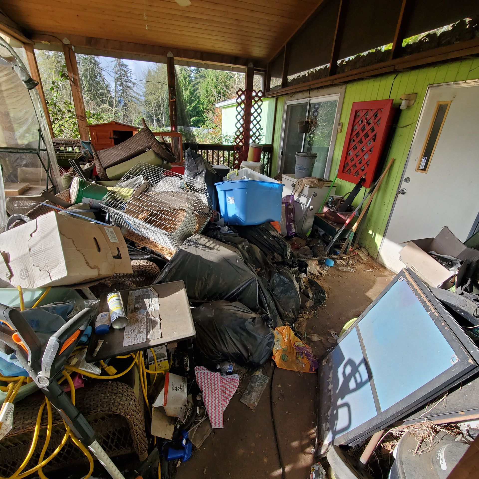 A cluttered porch with trash bags, cardboard boxes, and various items; the space appears to be unorganized.