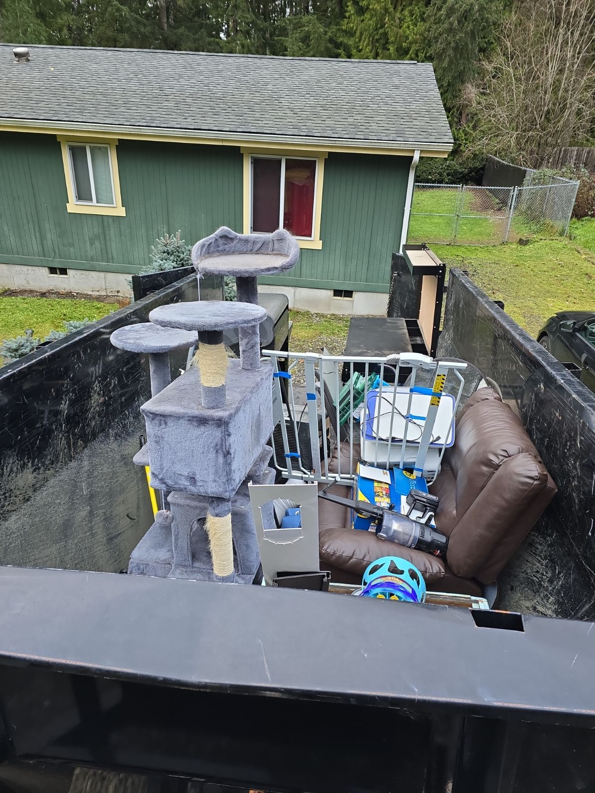 A dumpster filled with discarded items, including a cat tree, furniture, and various household items.