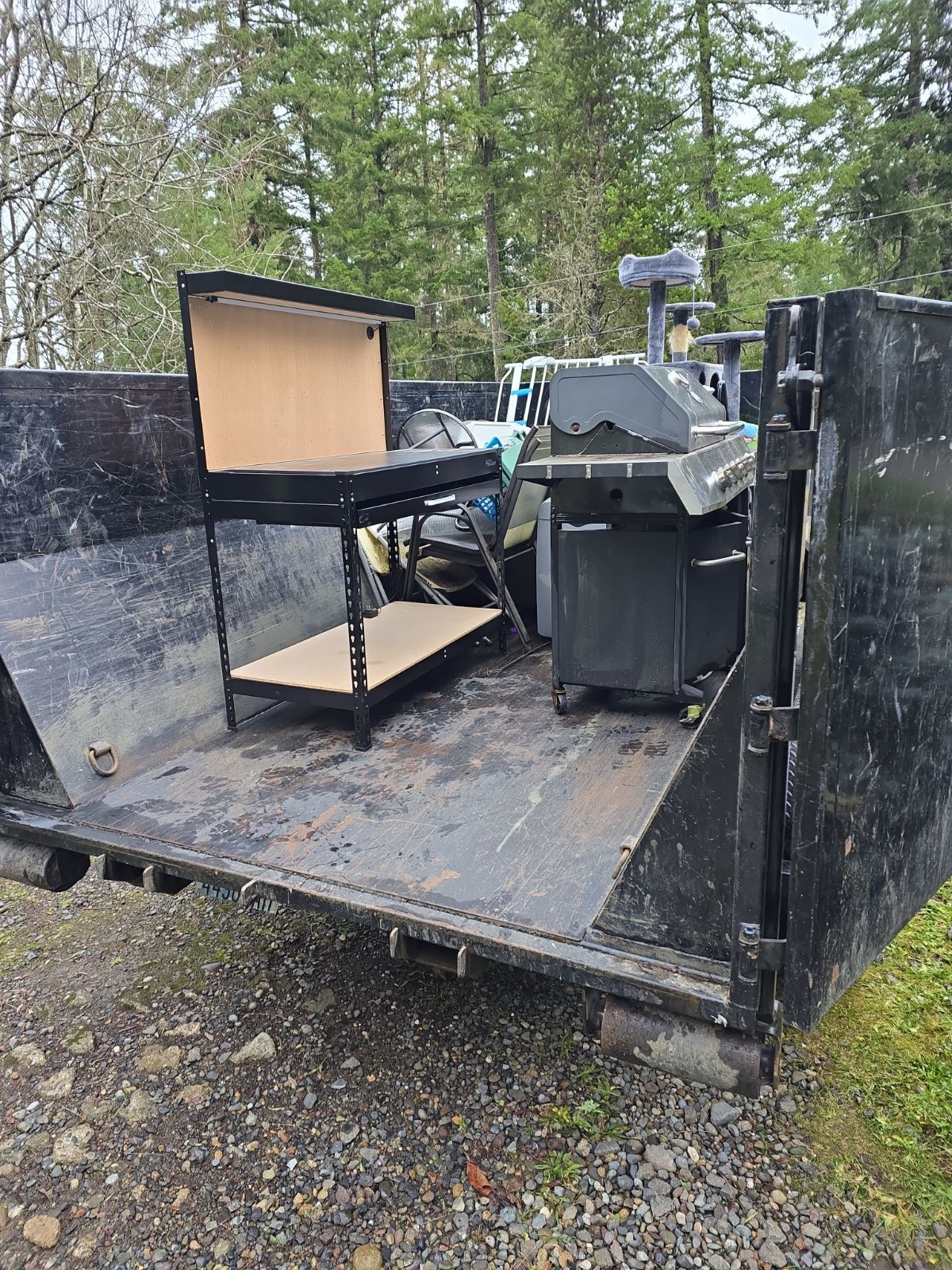A black dumpster with a black table and grill inside, parked outdoors.