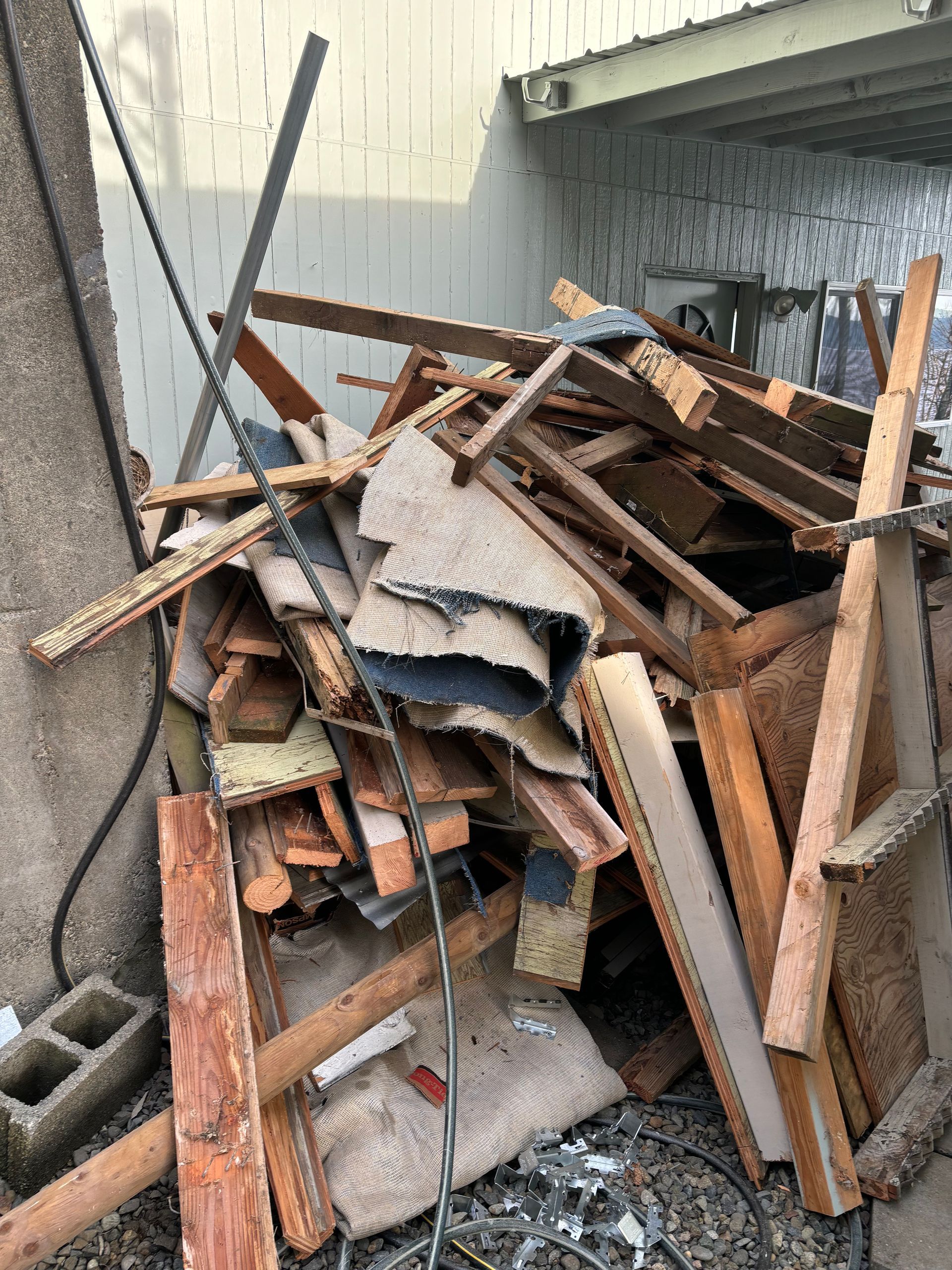 Pile of wood scraps, roofing, and debris against a wall.
