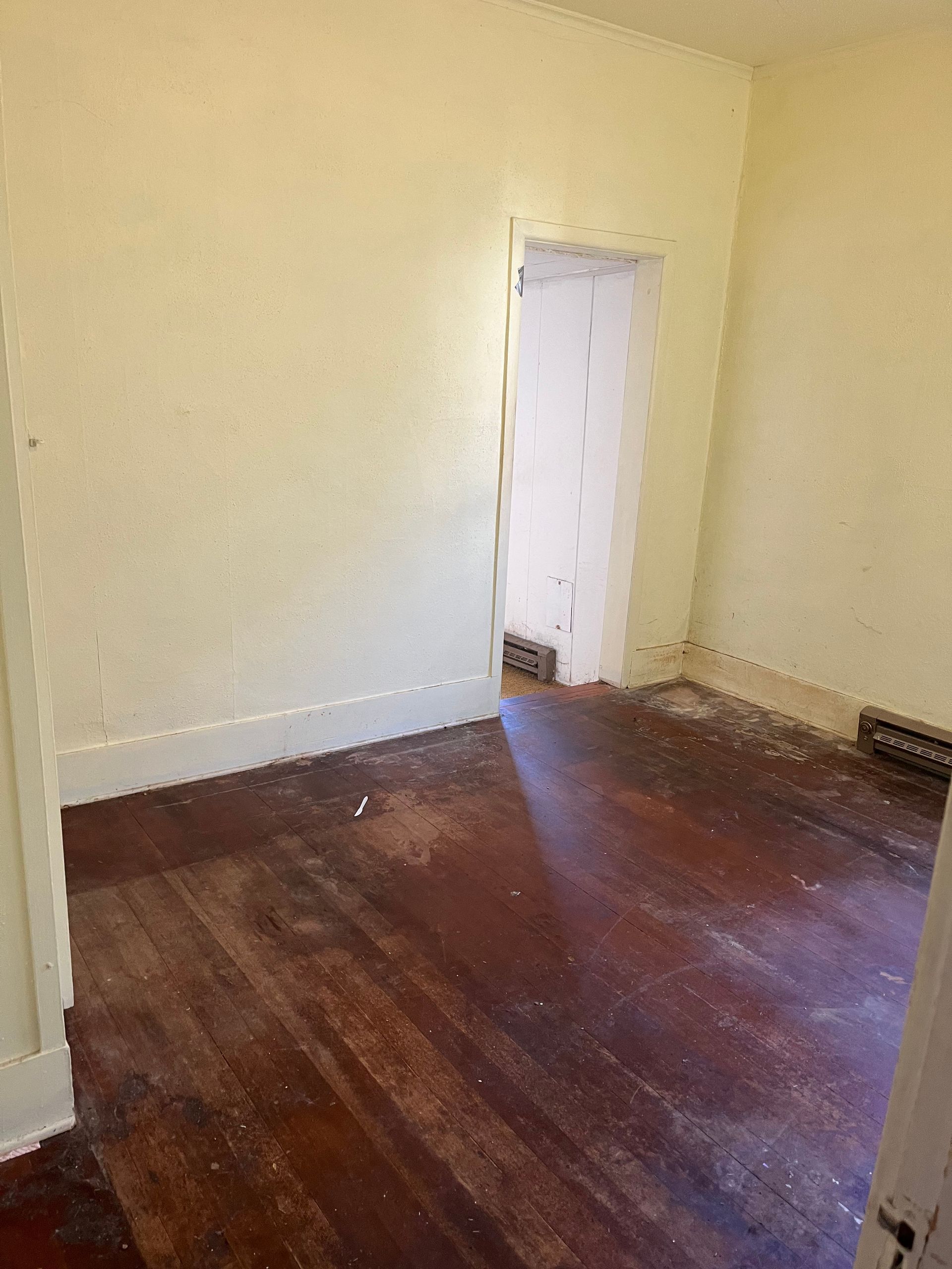 Empty room with stained hardwood floor, off-white walls, and a doorway.
