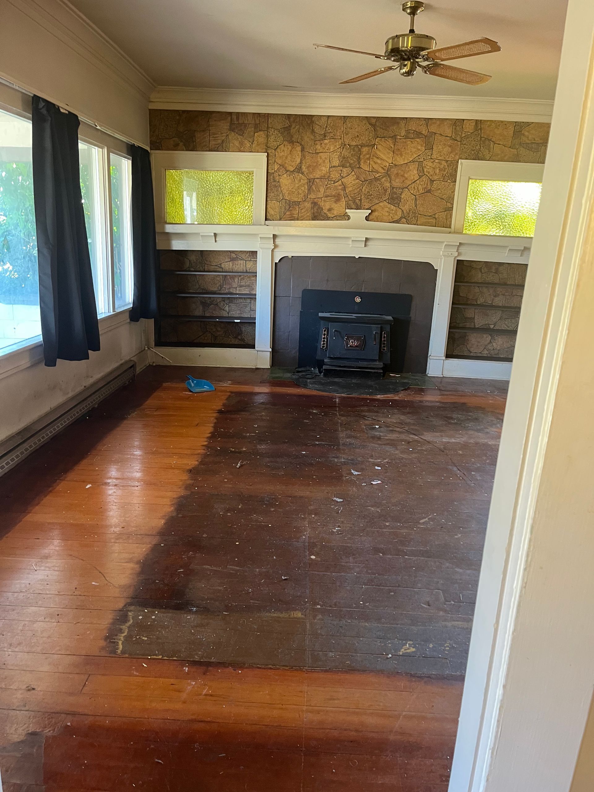 Empty living room with fireplace and hardwood floors. Dark curtains hang on the left side.