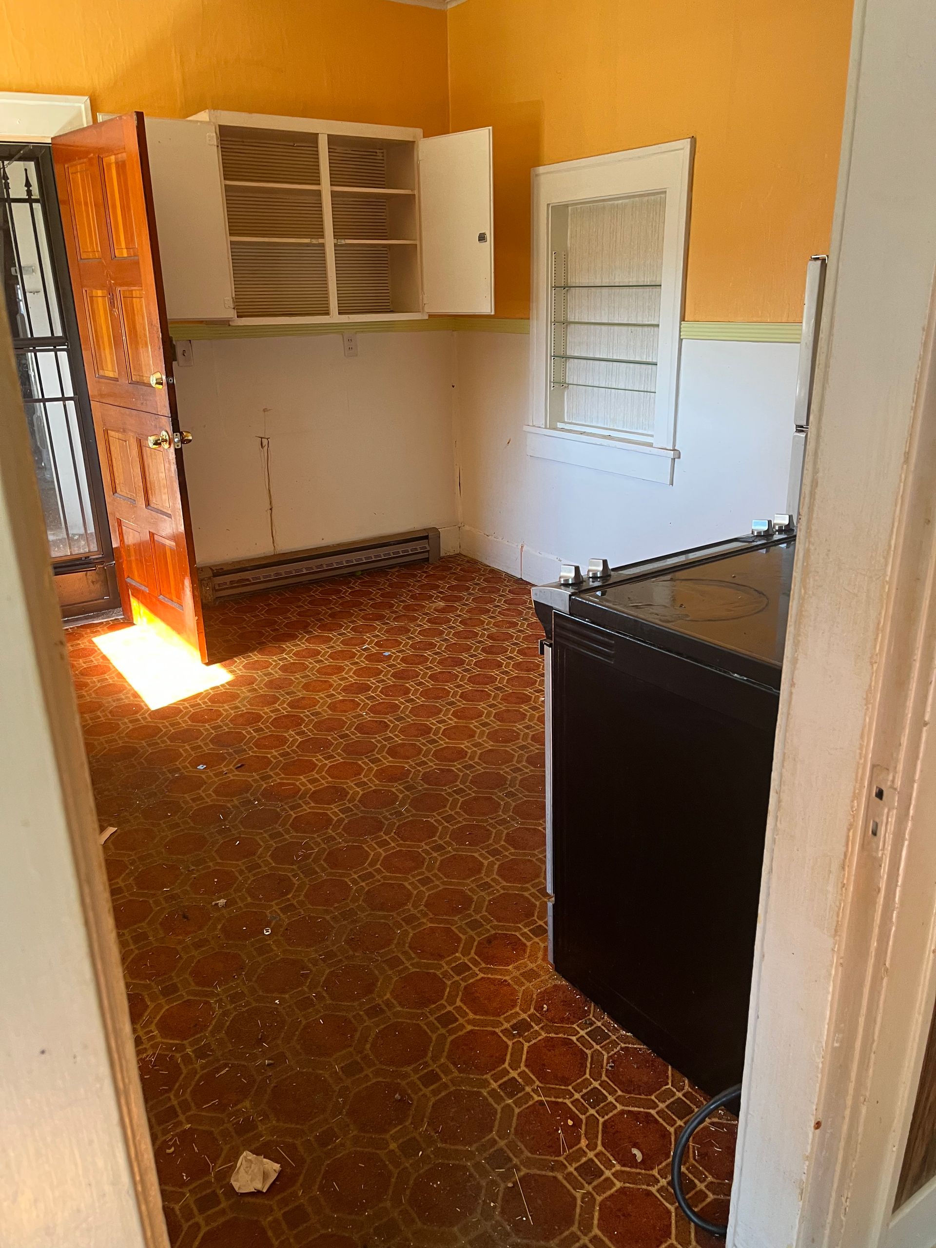 Orange kitchen with damaged floor, cabinets, and appliance.
