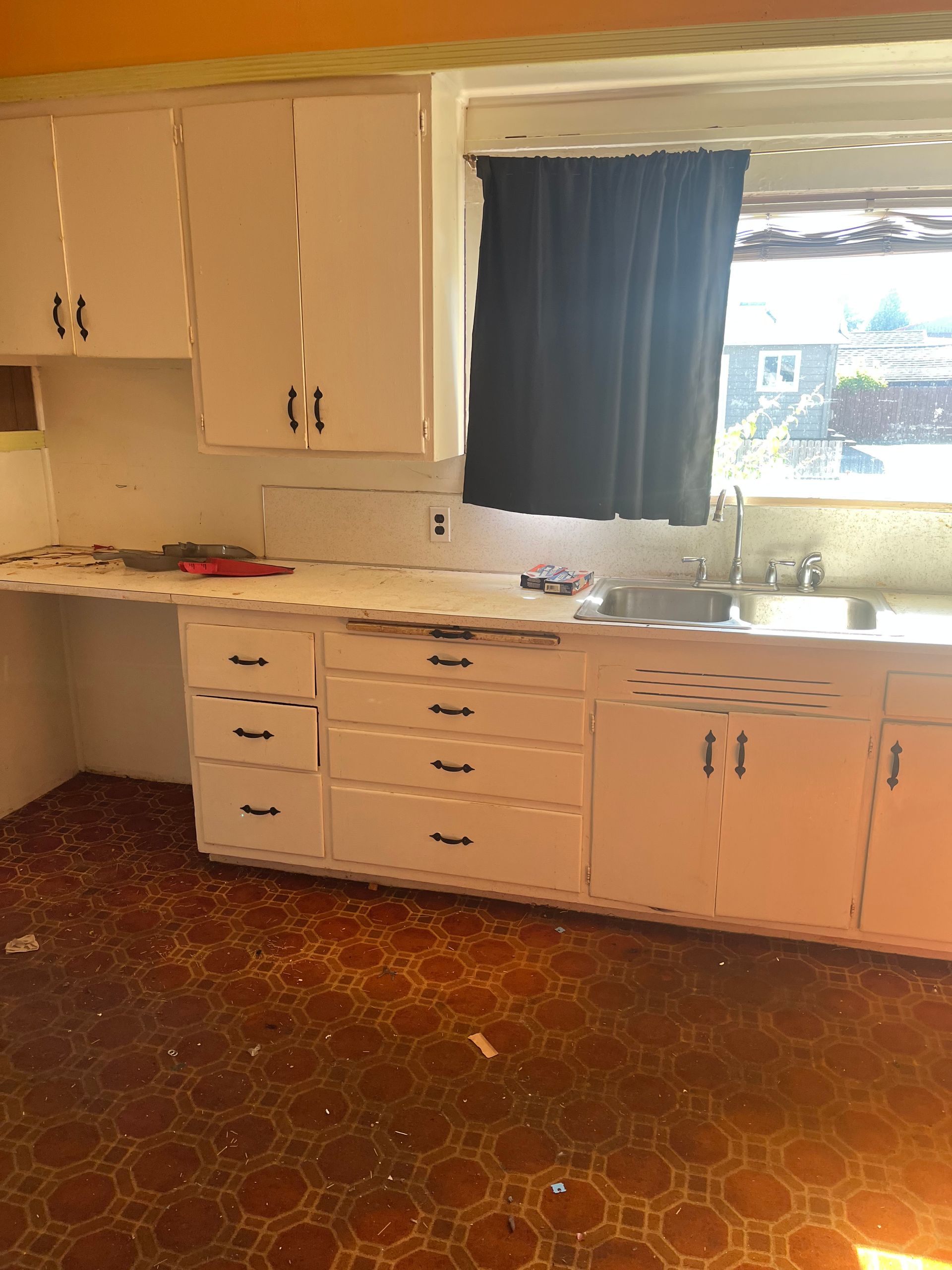 White kitchen cabinets with black hardware and a window above the sink; the floor is brown patterned.