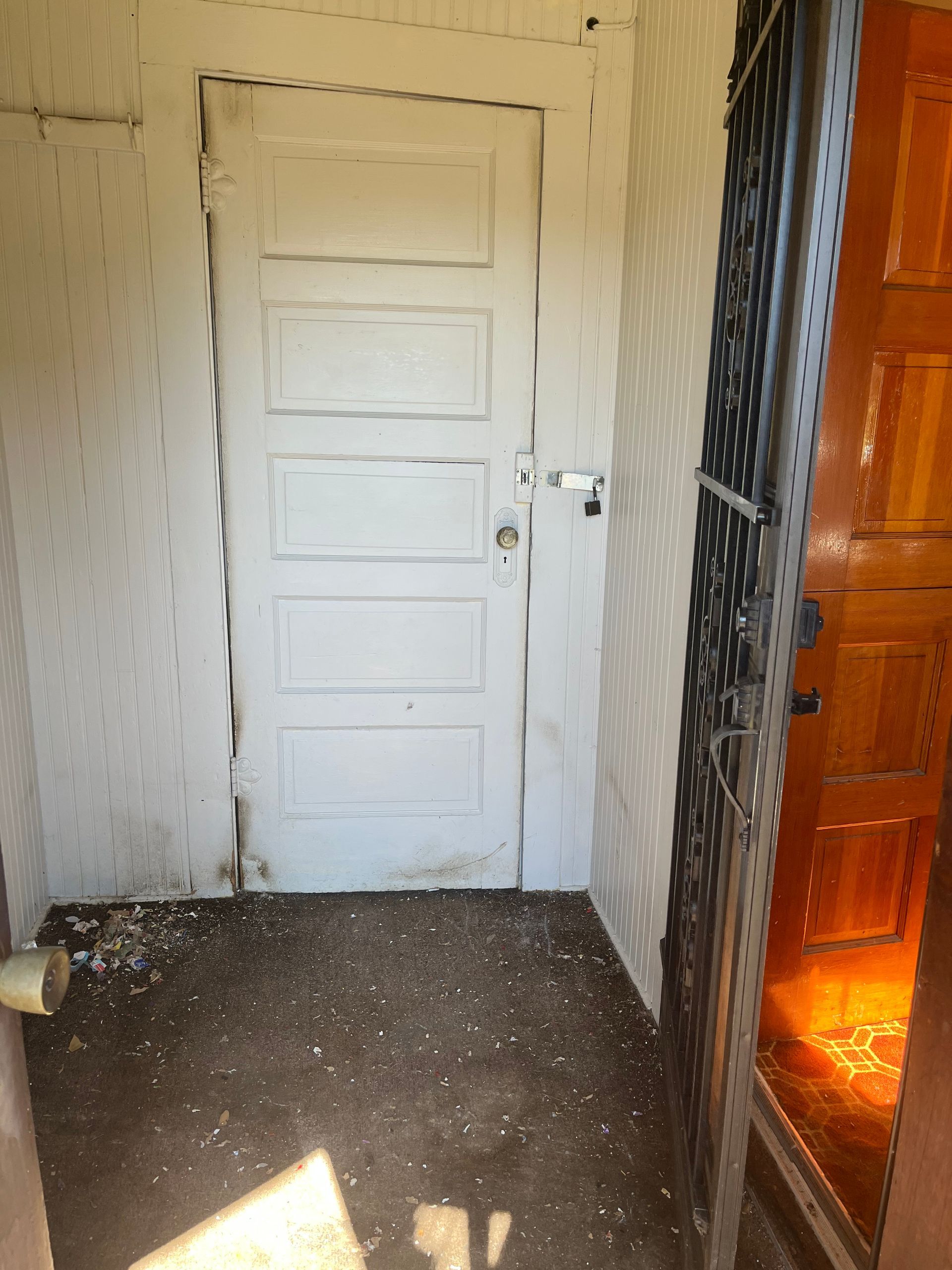 White door with black security gate and debris on the floor in an entryway.