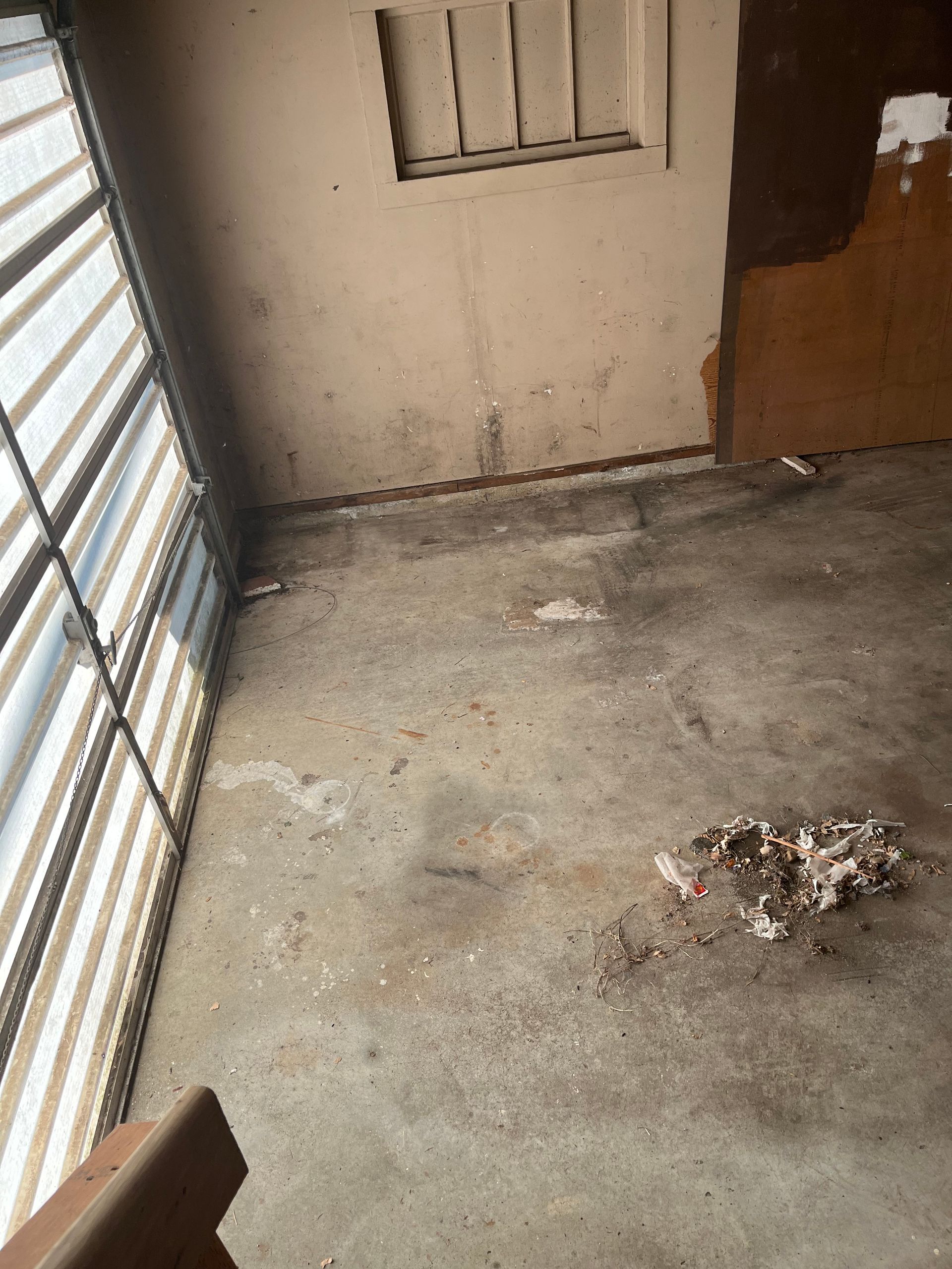 Concrete floor in room with window, dirty walls, and debris.