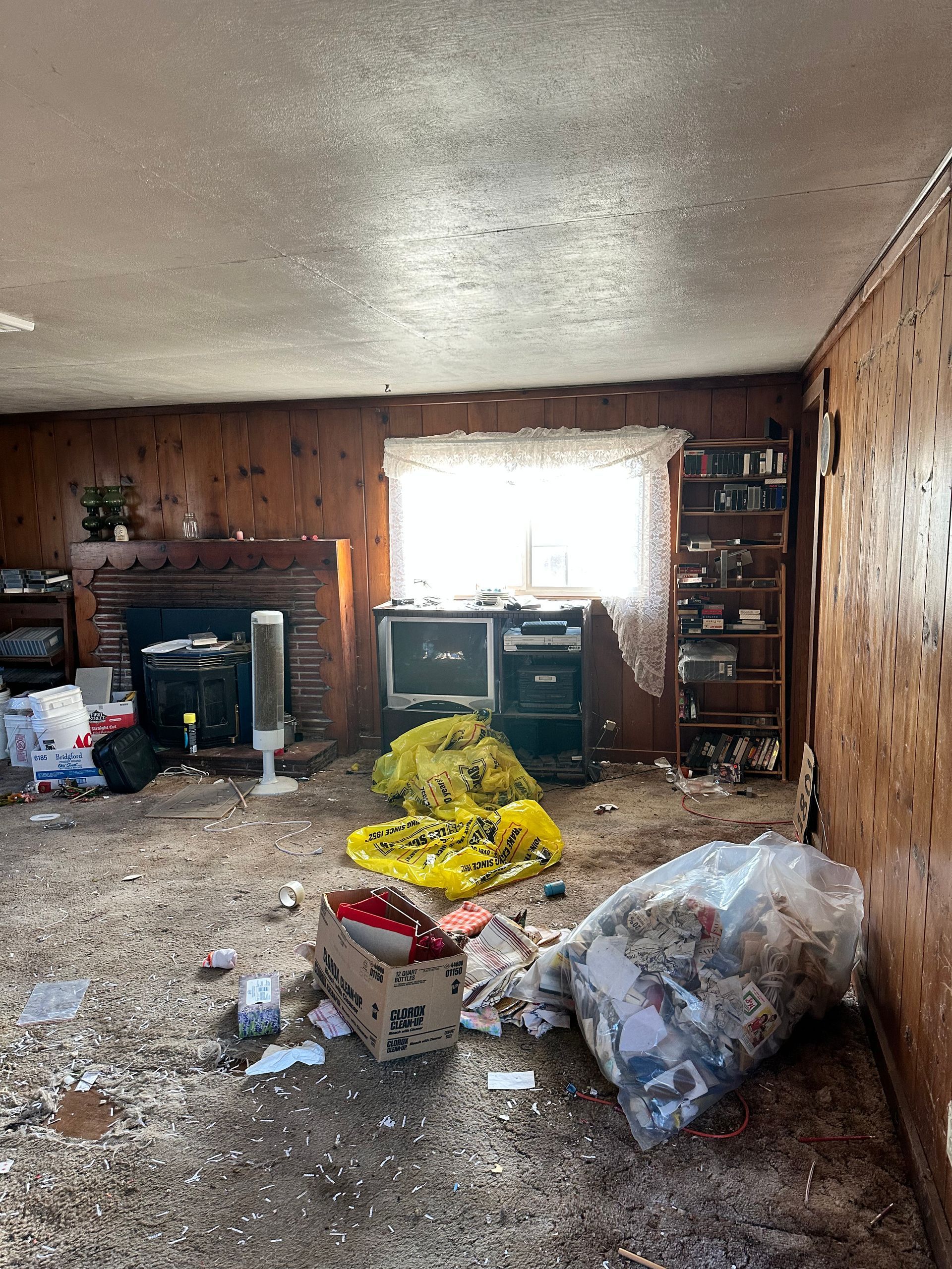 Messy room with trash, paneled walls, and a window.