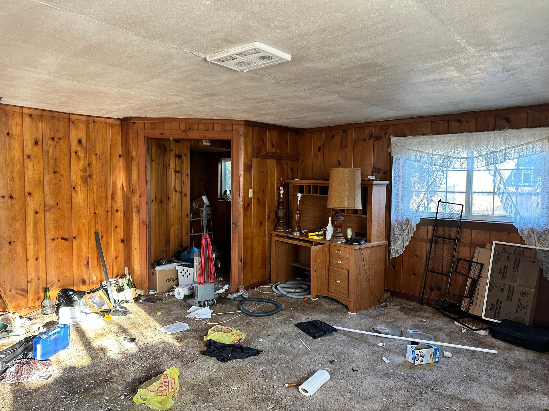 Cluttered room with wood paneling and debris on the floor. A desk and doorway are visible.