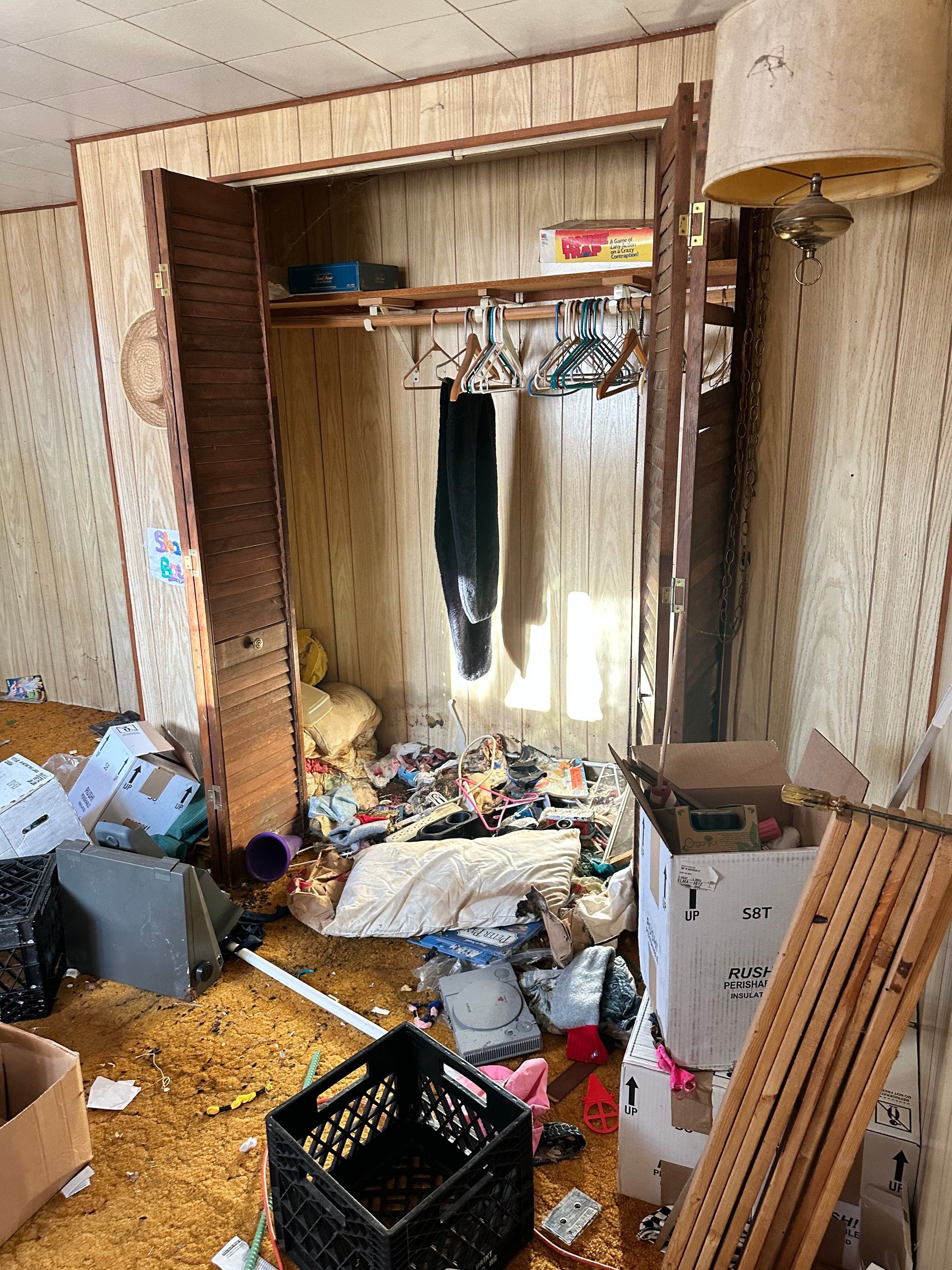Messy room with open closet and debris on the floor. Yellow carpet, cluttered storage.