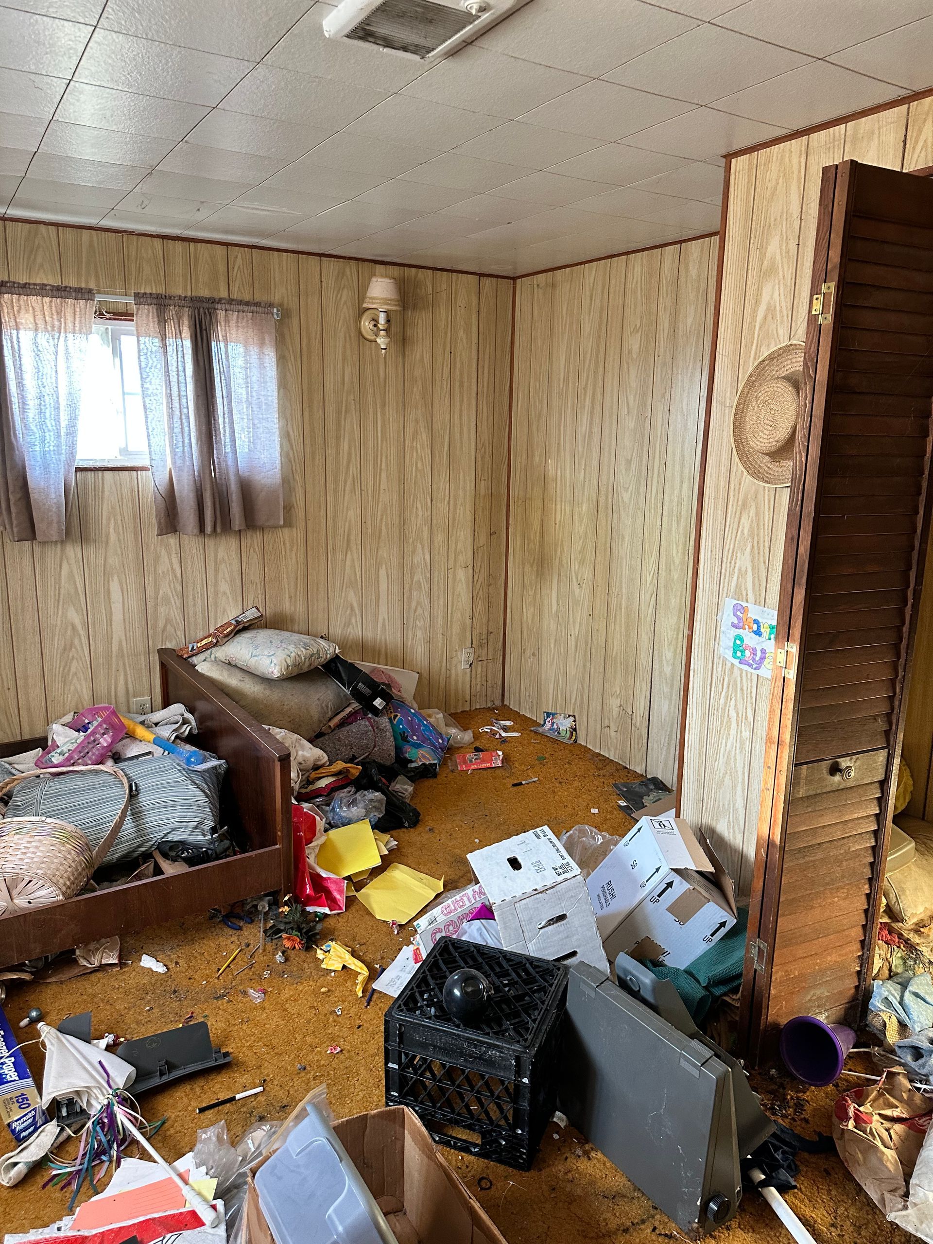 Messy room with dirty carpet, boxes, and items scattered everywhere, including a bed.
