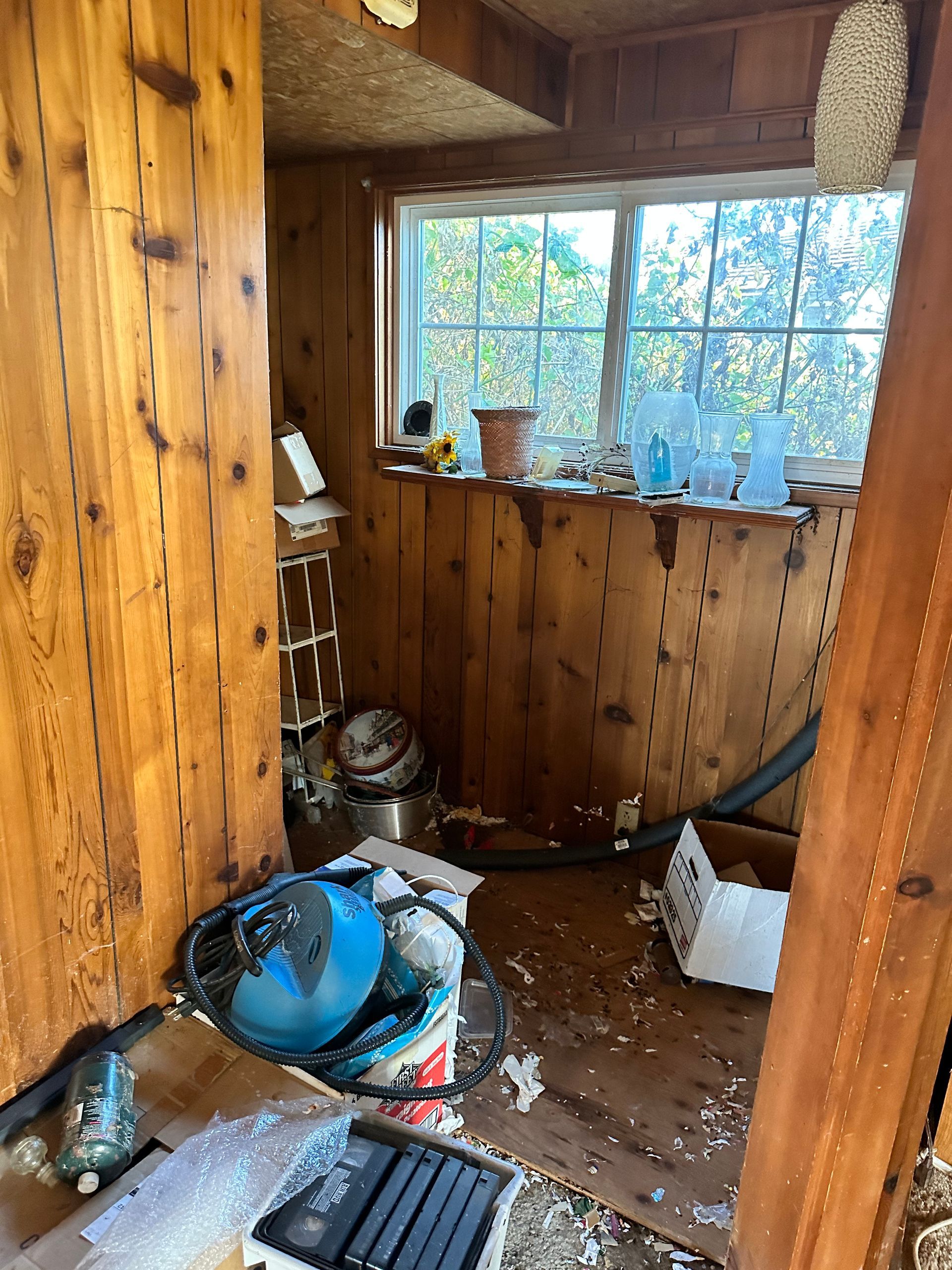 A cluttered, wood-paneled room with a window. Debris and objects cover the floor.