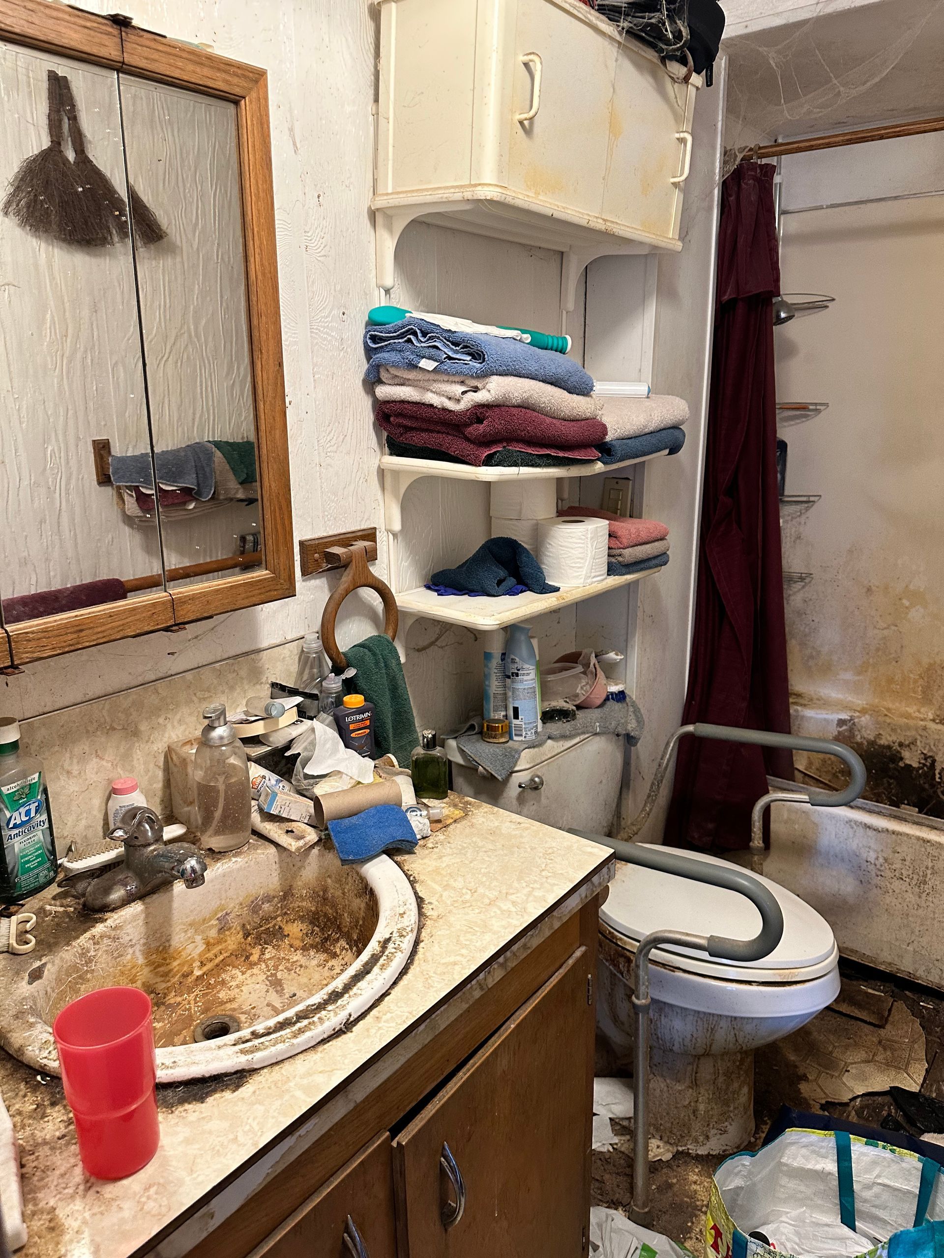 Dirty bathroom with stained walls and fixtures. A sink, toilet, and shower are visible.