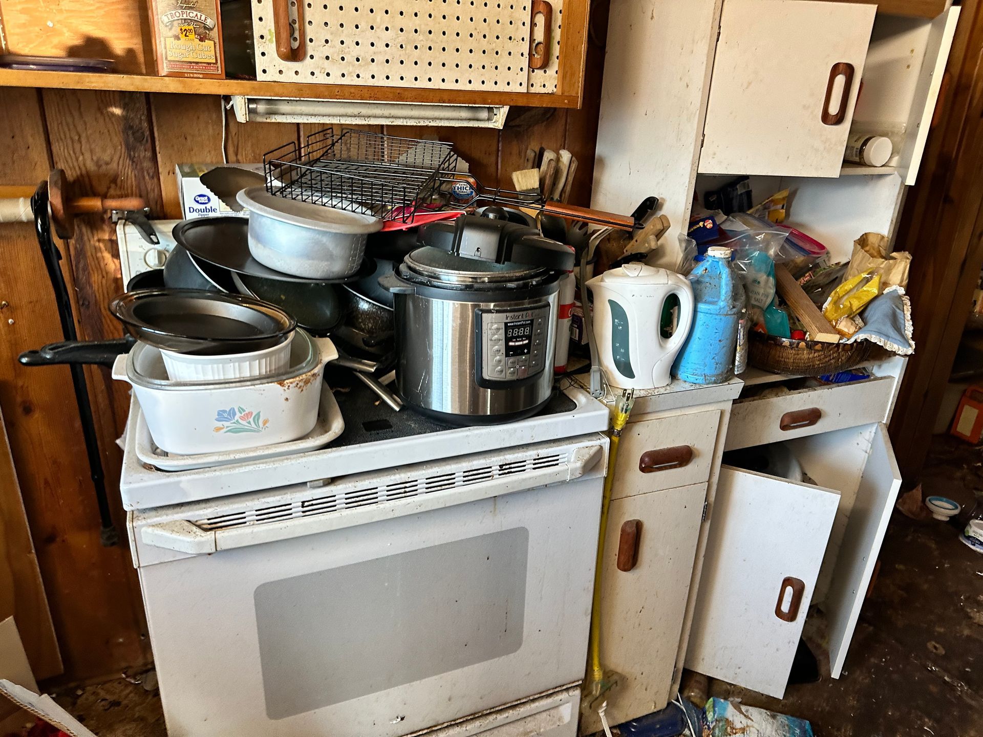 Messy kitchen with appliances and cluttered countertops. White stove, Instant Pot, and overflowing cabinets.