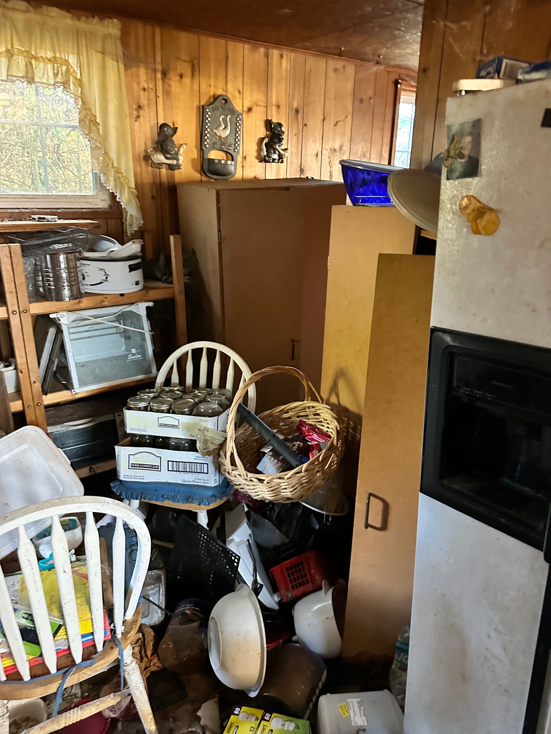 Cluttered room with wooden walls, appliances, and miscellaneous items; a chair in foreground.