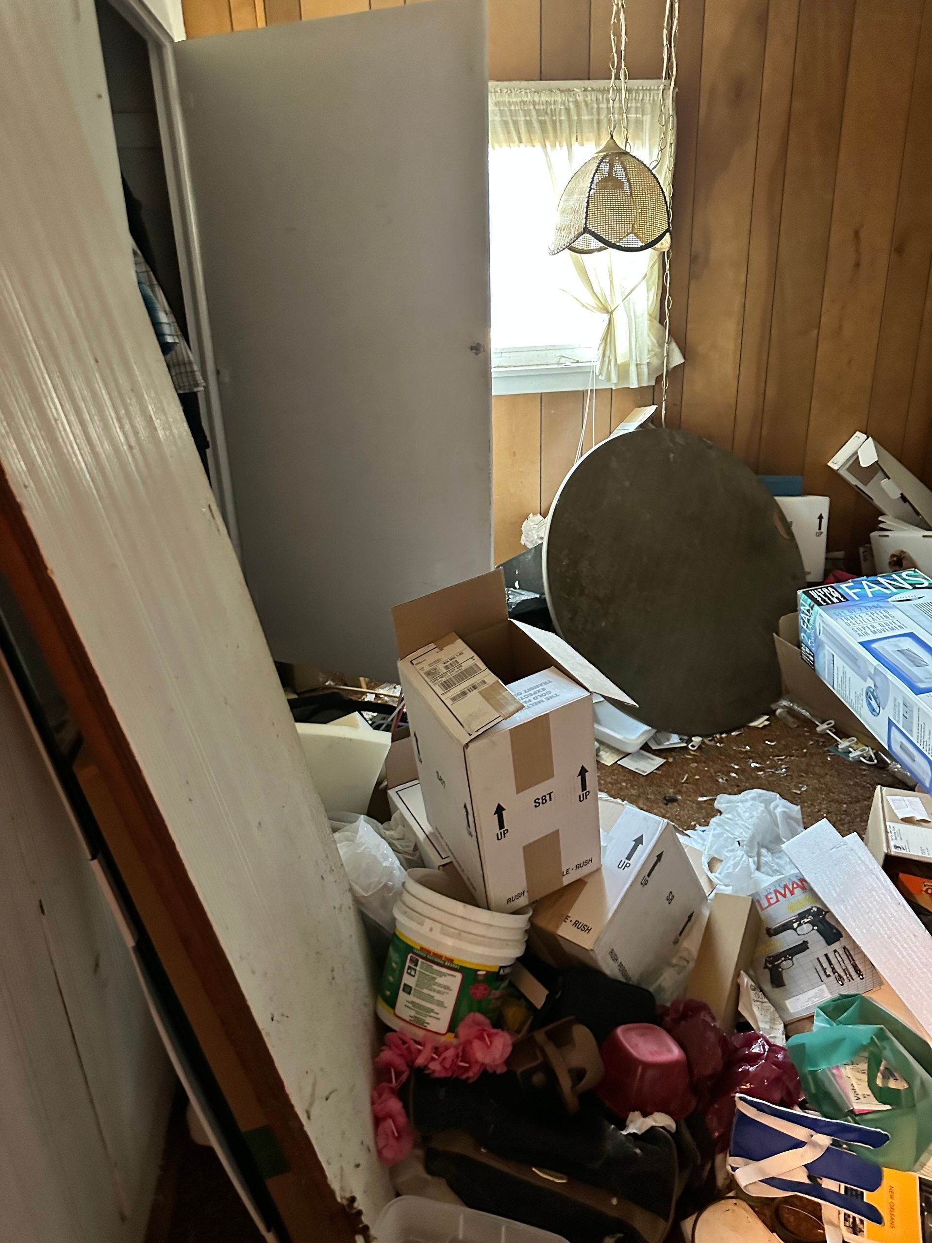 Cluttered room; boxes, debris, and items scattered on floor. A door and window visible.