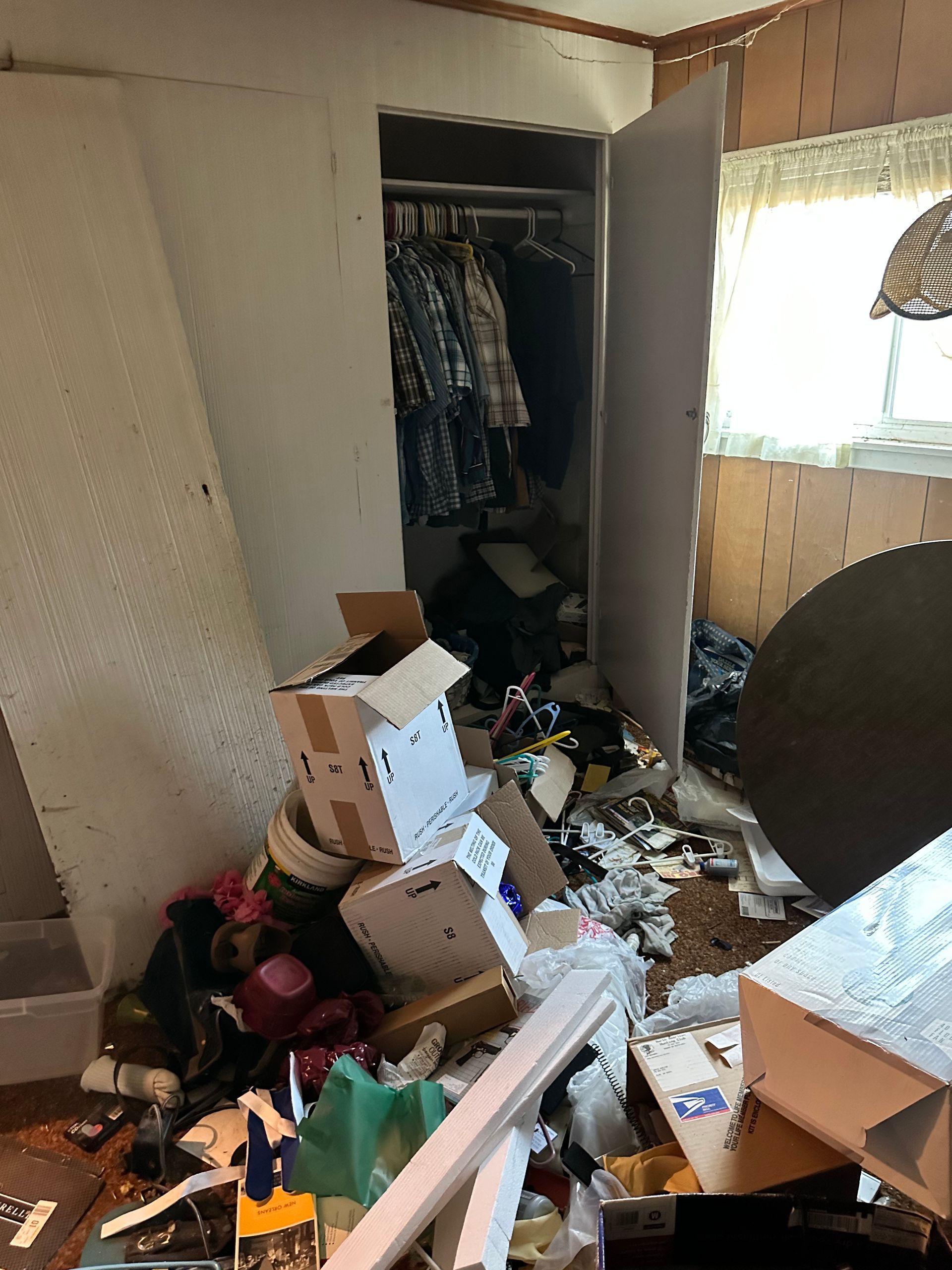 Cluttered room with open closet; boxes and debris on the floor; window to the right.