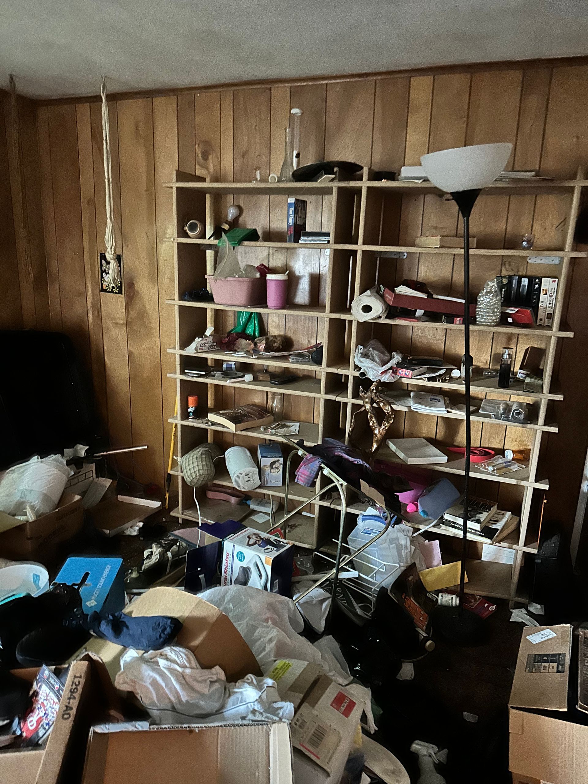 Cluttered room with shelves, boxes, and various items. Brown paneling on the wall.