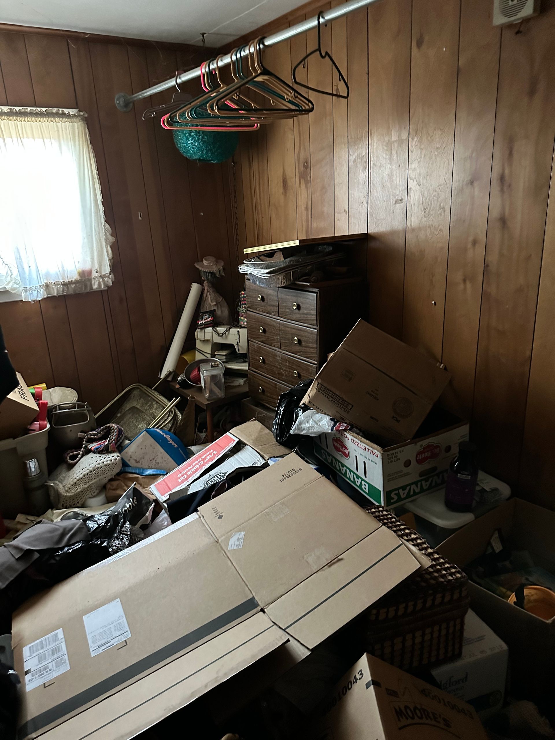 Cluttered room with cardboard boxes, furniture, and miscellaneous items scattered around.
