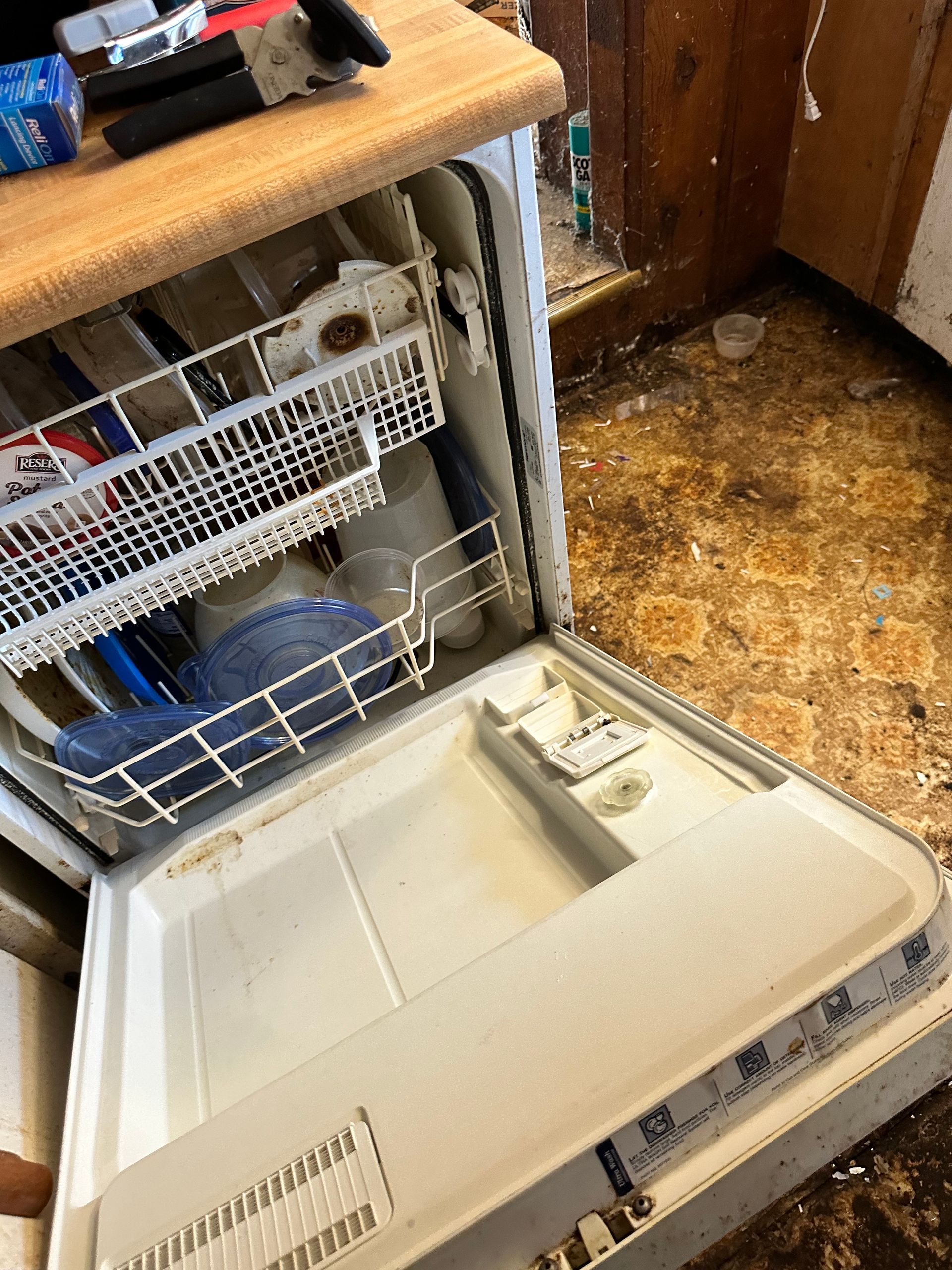 Dishwasher door open, interior showing dirty dishes. Kitchen floor appears stained.