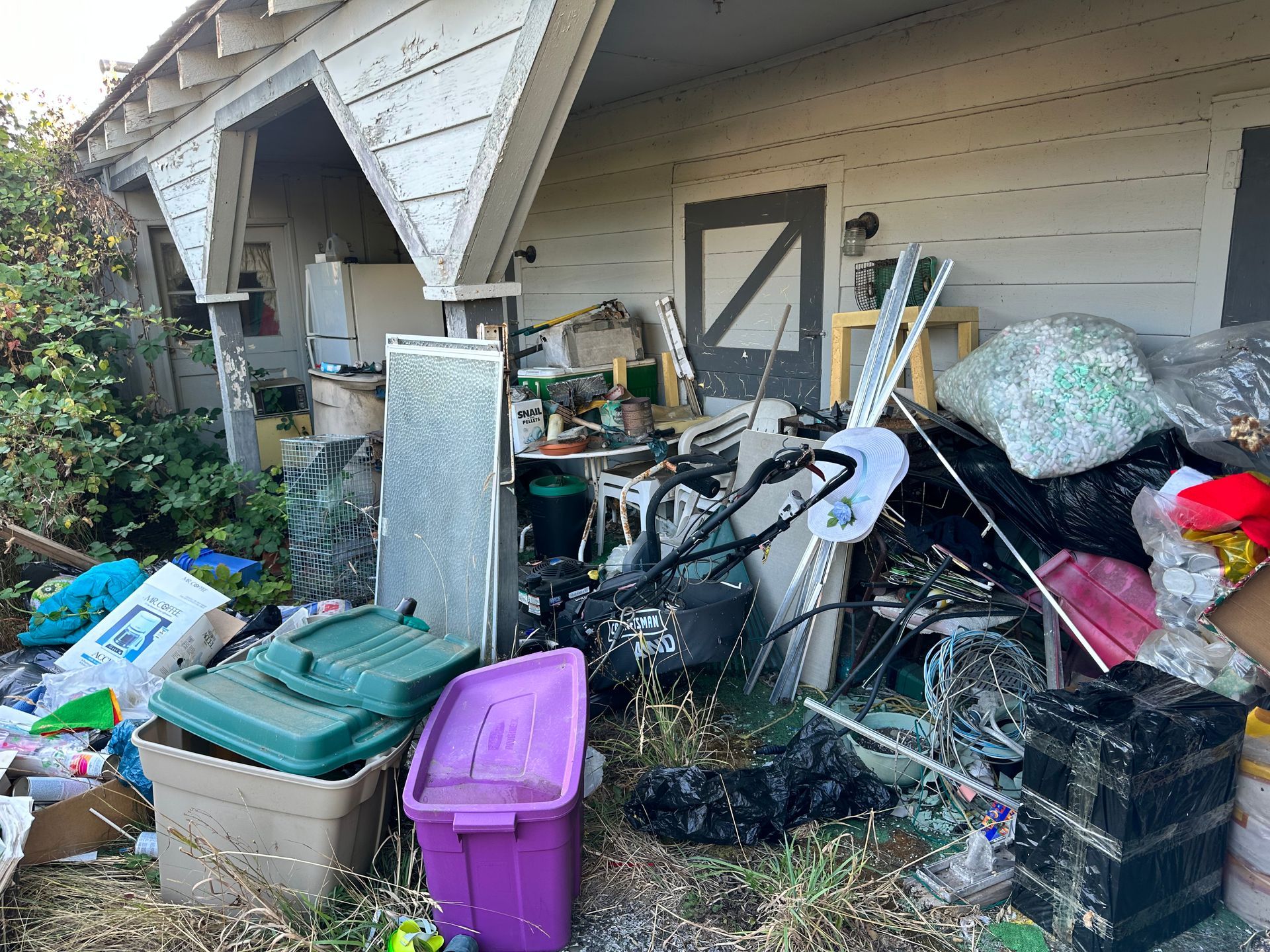 Exterior of a cluttered building with trash, a refrigerator, and containers.