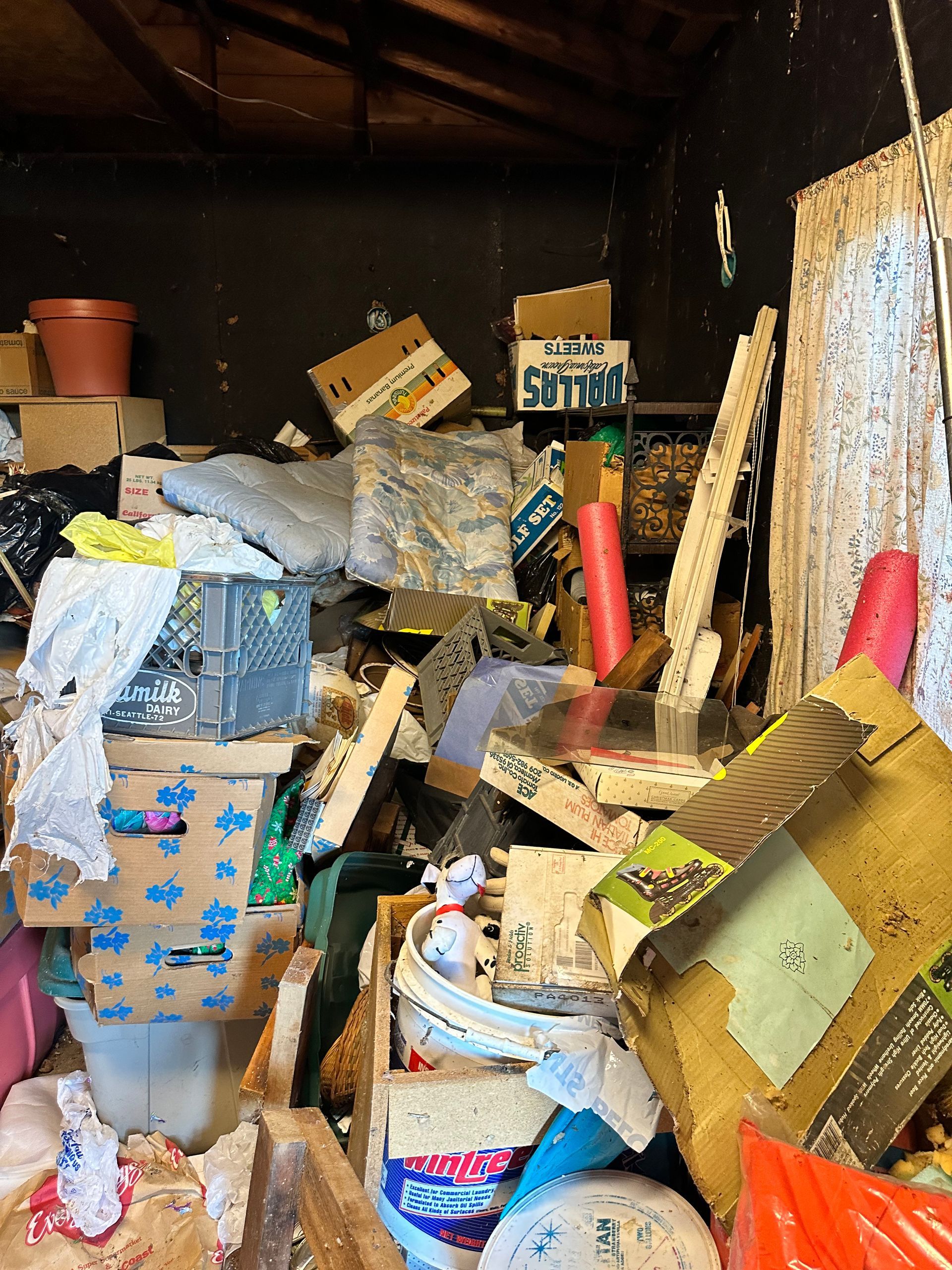 Messy storage room: boxes, objects piled haphazardly; beige, brown, pink, white colors.