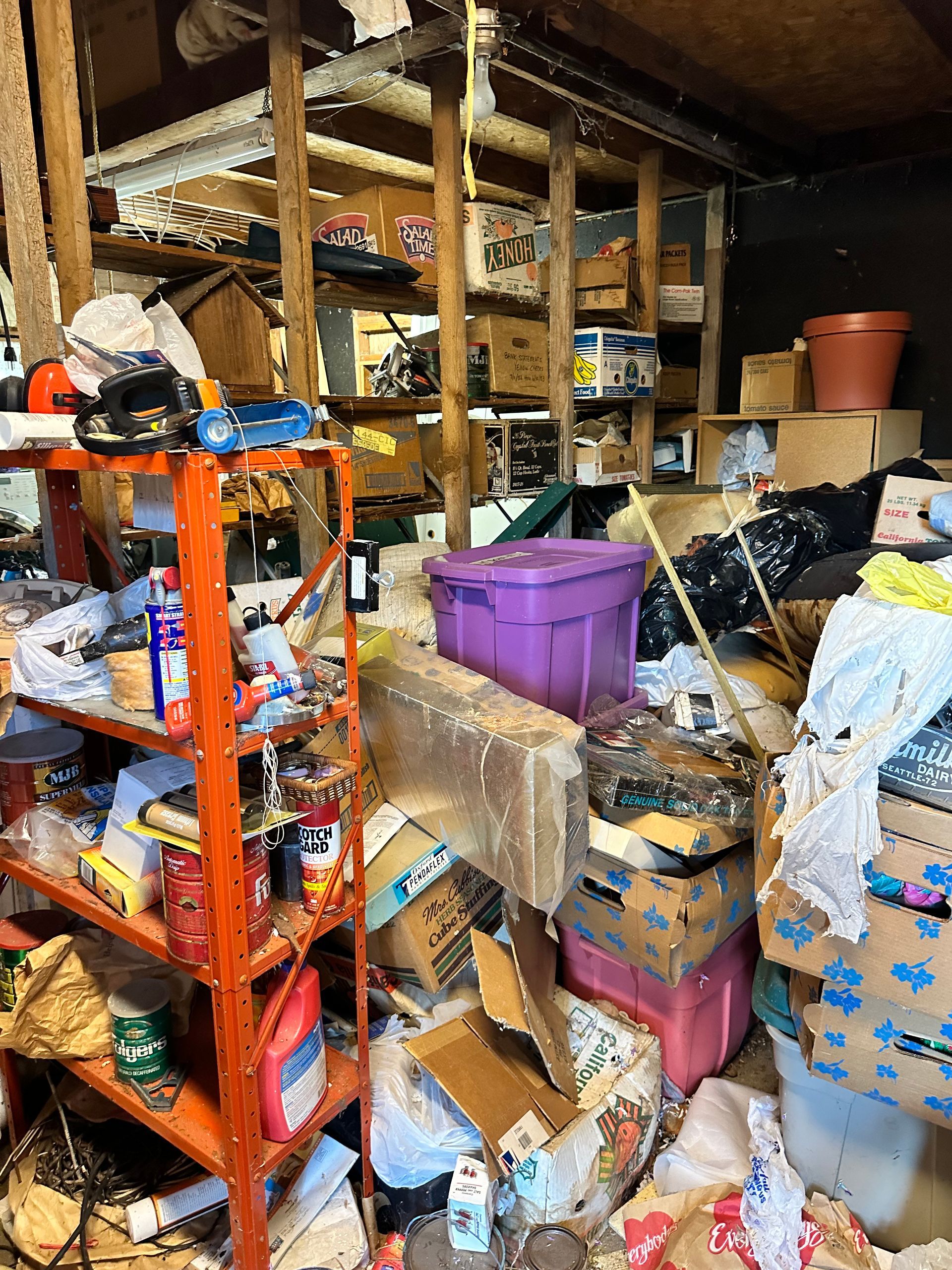 Cluttered garage with red shelving, boxes, and general disarray. Purple bin in the center.