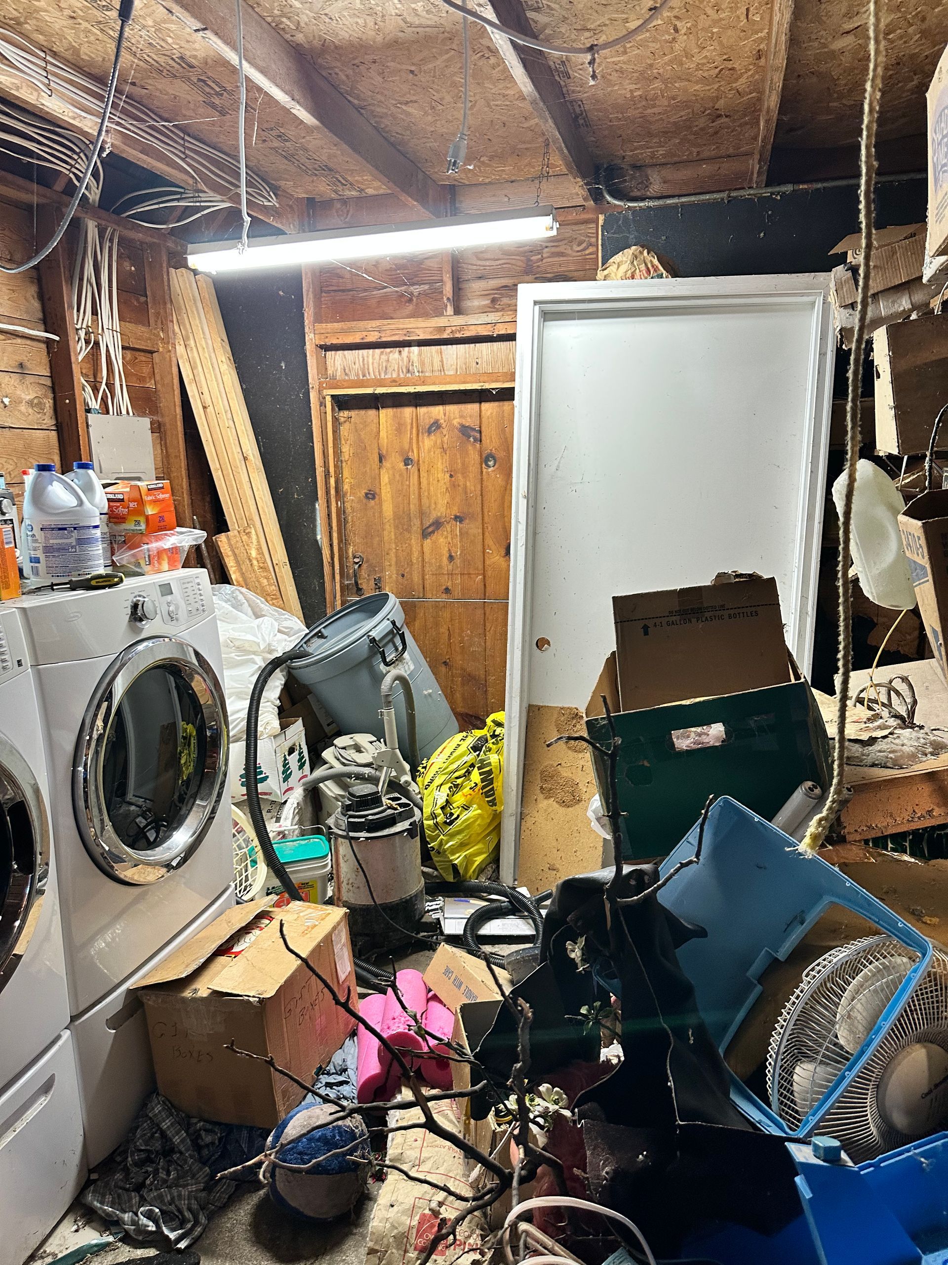 Cluttered basement: washer/dryer, boxes, debris, closed white door, and wooden door.