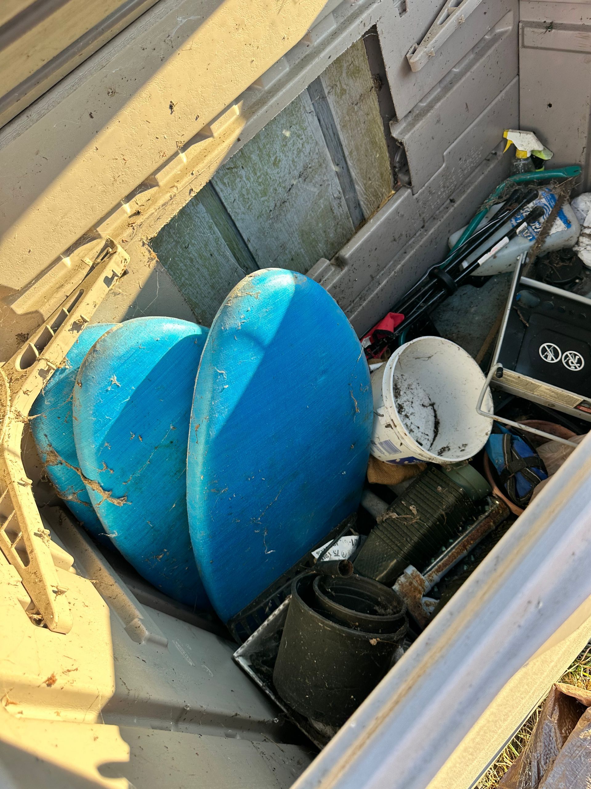 A cluttered, open storage bin containing blue foam pads, a white container, and miscellaneous items.