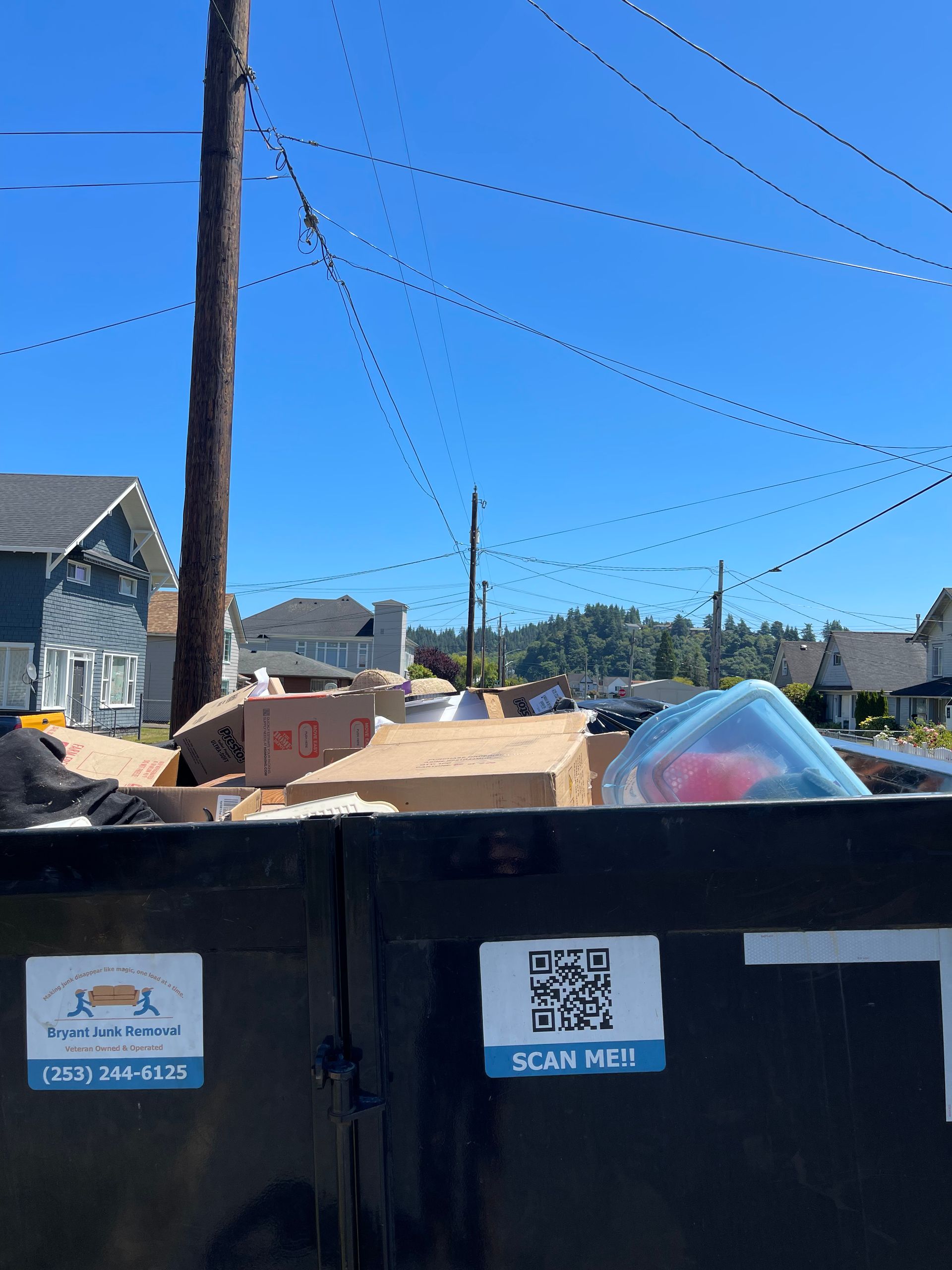 Dumpster filled with cardboard boxes, a plastic container, and a sticker that says 